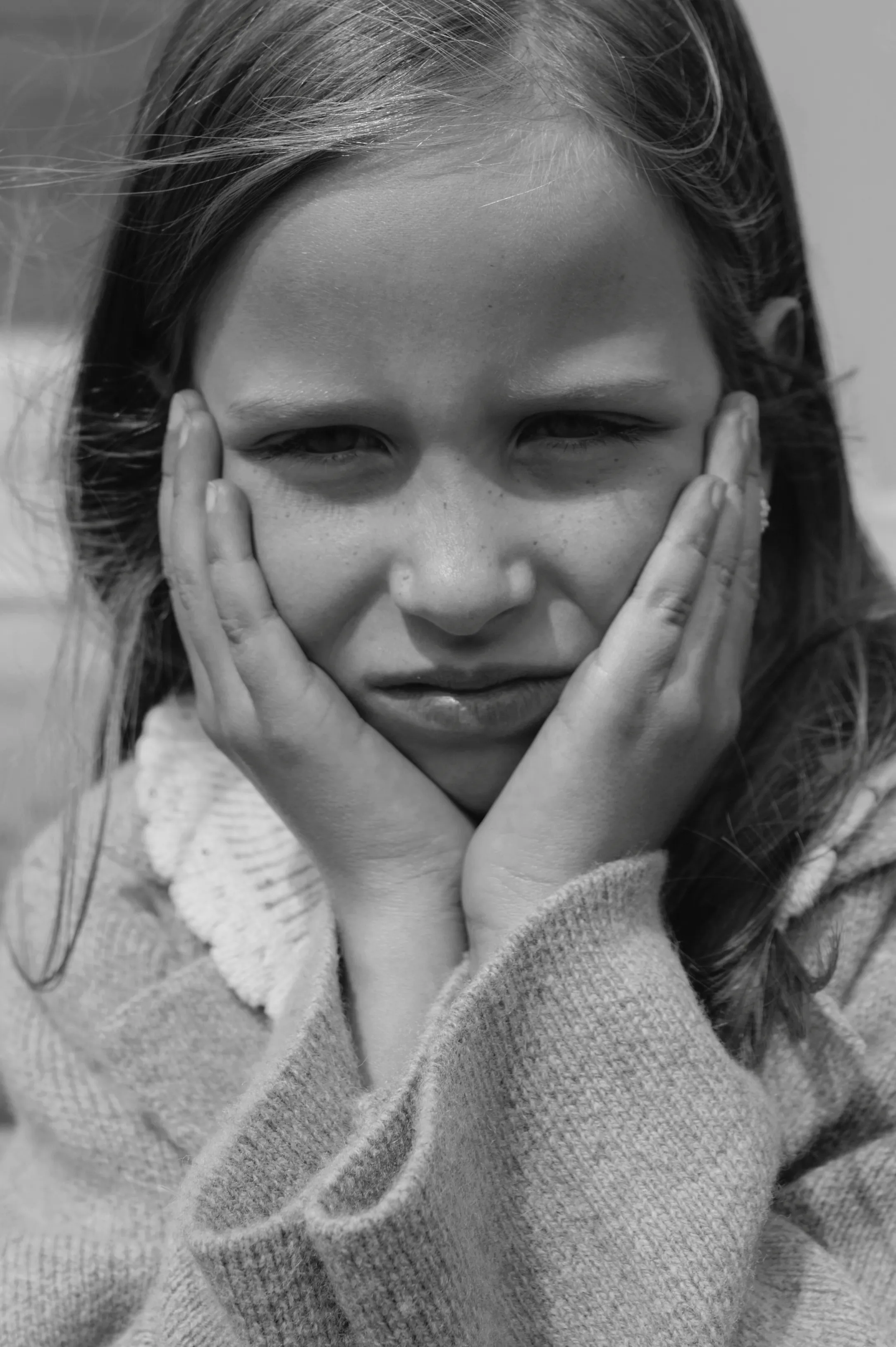 Black-and-white close portrait of a child resting their face in their hands, with soft blurred background.