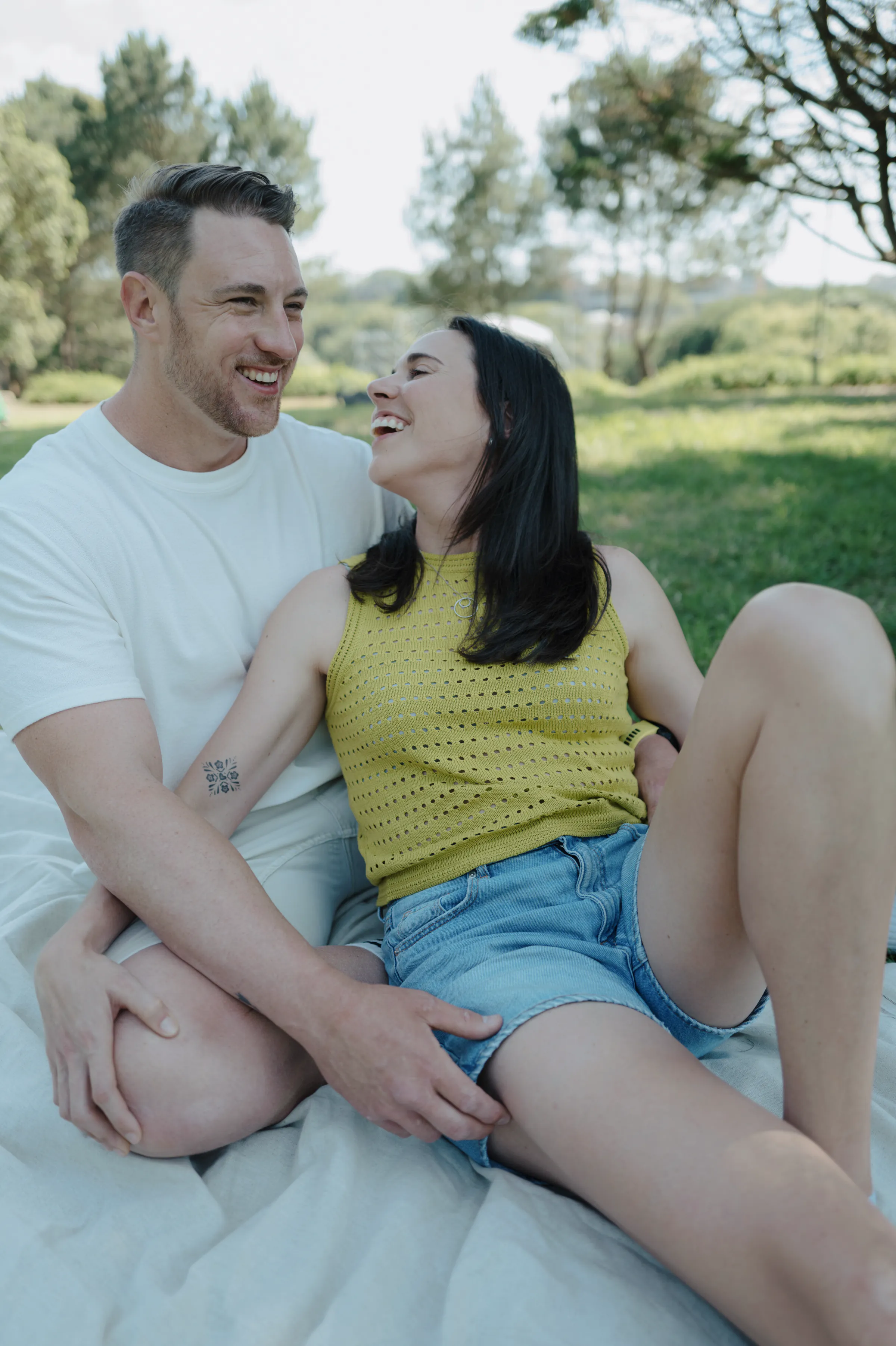 Couple seated close on a blanket during a relaxed park portrait session in soft daylight