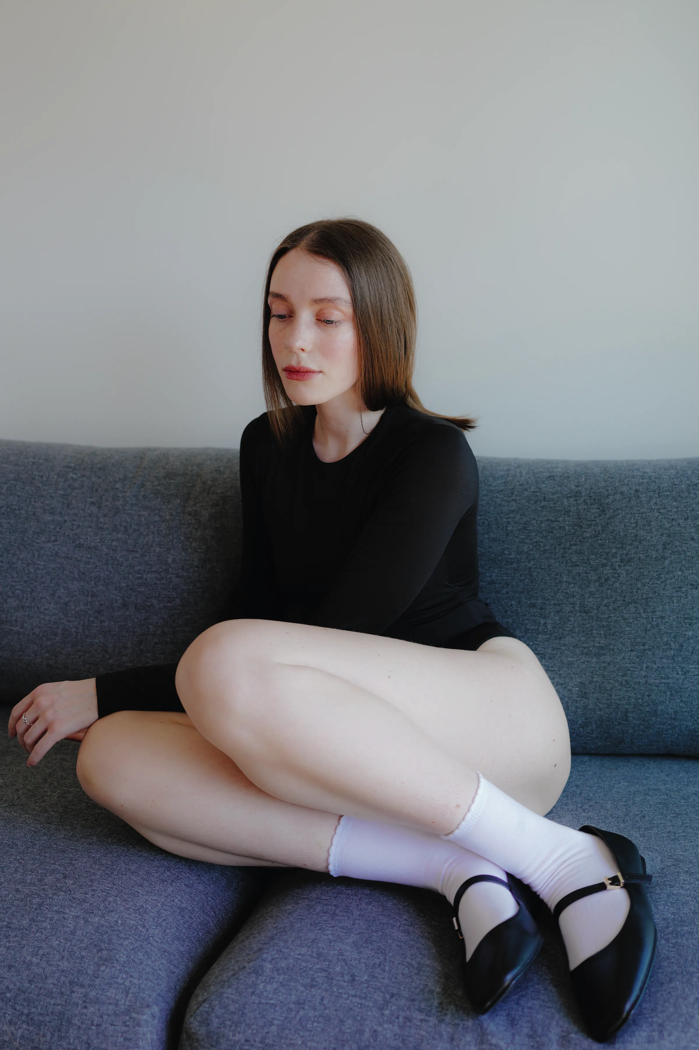 Indoor portrait of a person seated curled on a gray sofa in soft light.