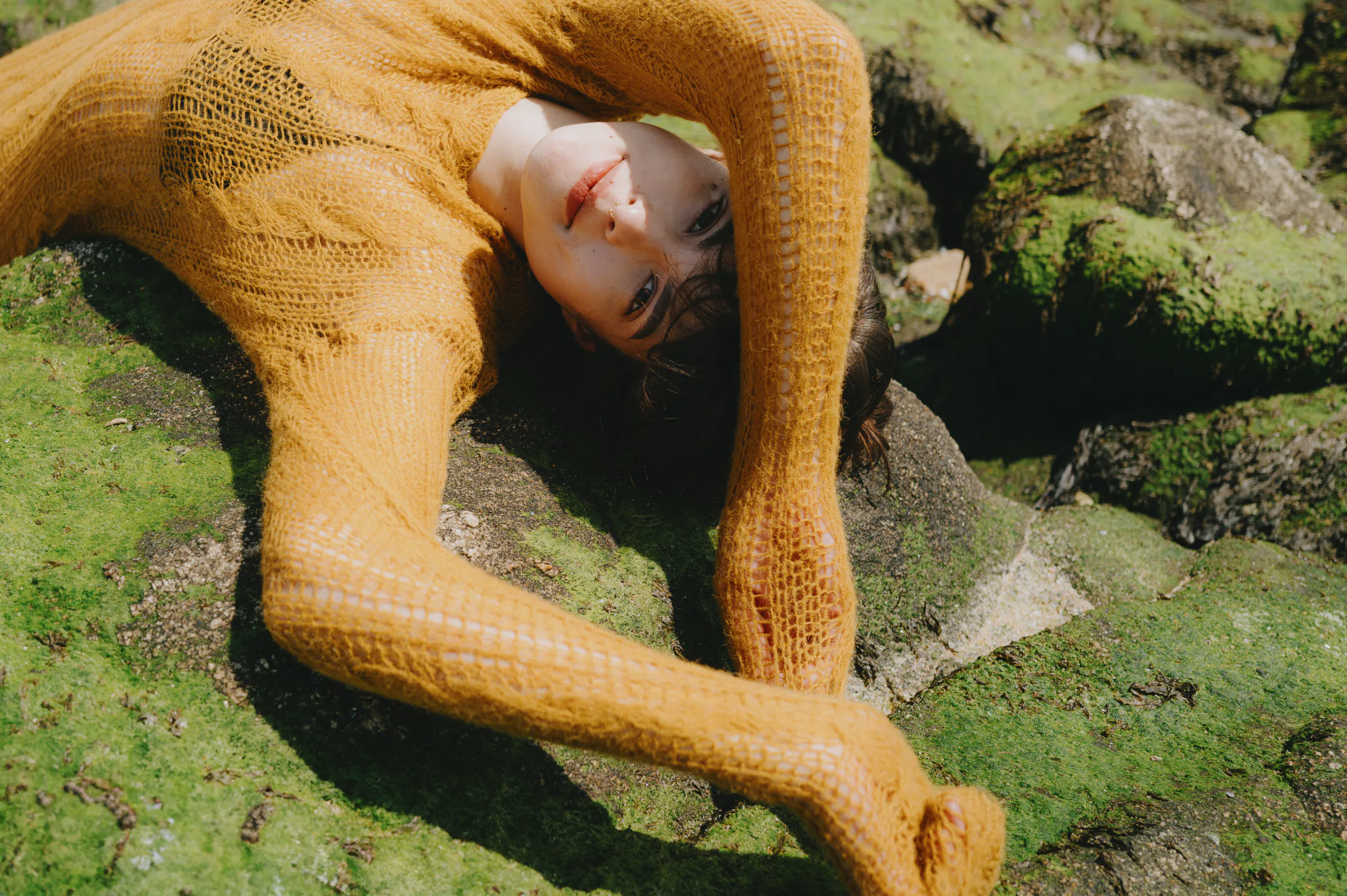 Close portrait of a person in a mustard knit sweater lying on mossy rocks outdoors.