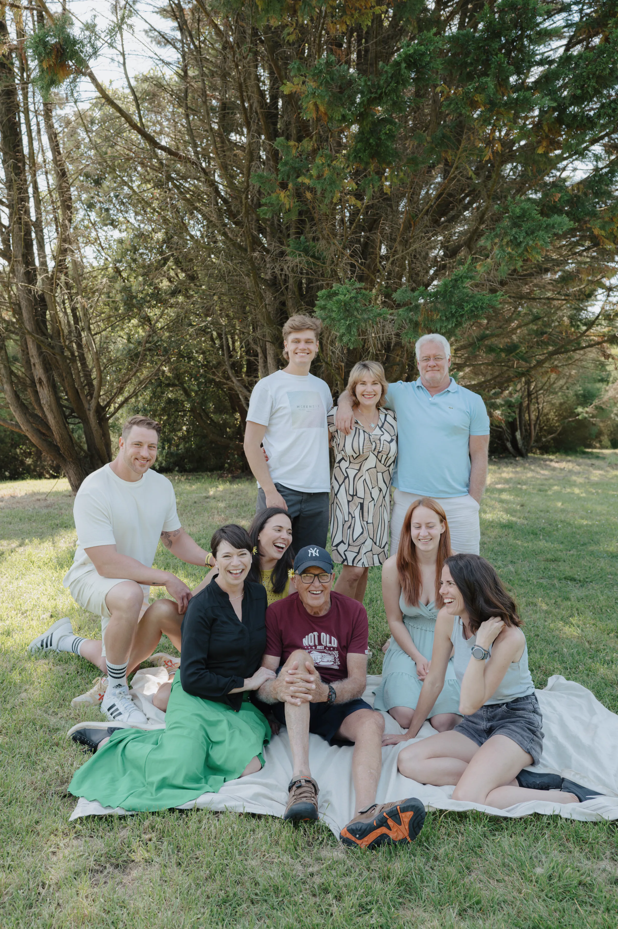 Group portrait during an outdoor session on grass beneath tall trees in soft light.