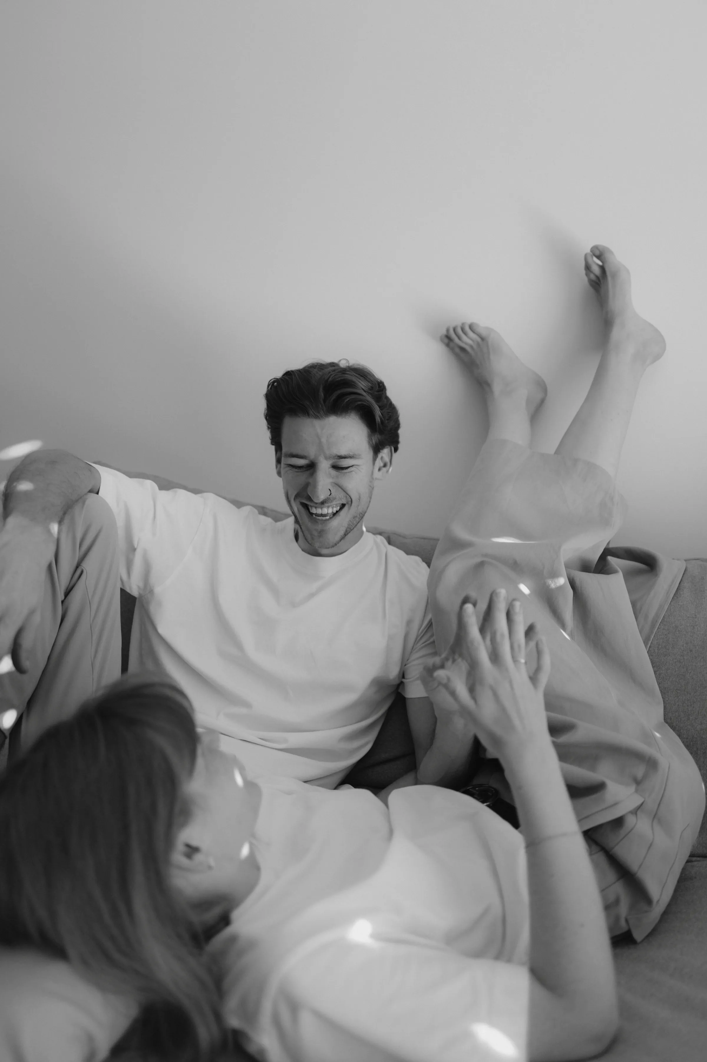 Black-and-white home session with a family relaxing playfully on a sofa in soft light.
