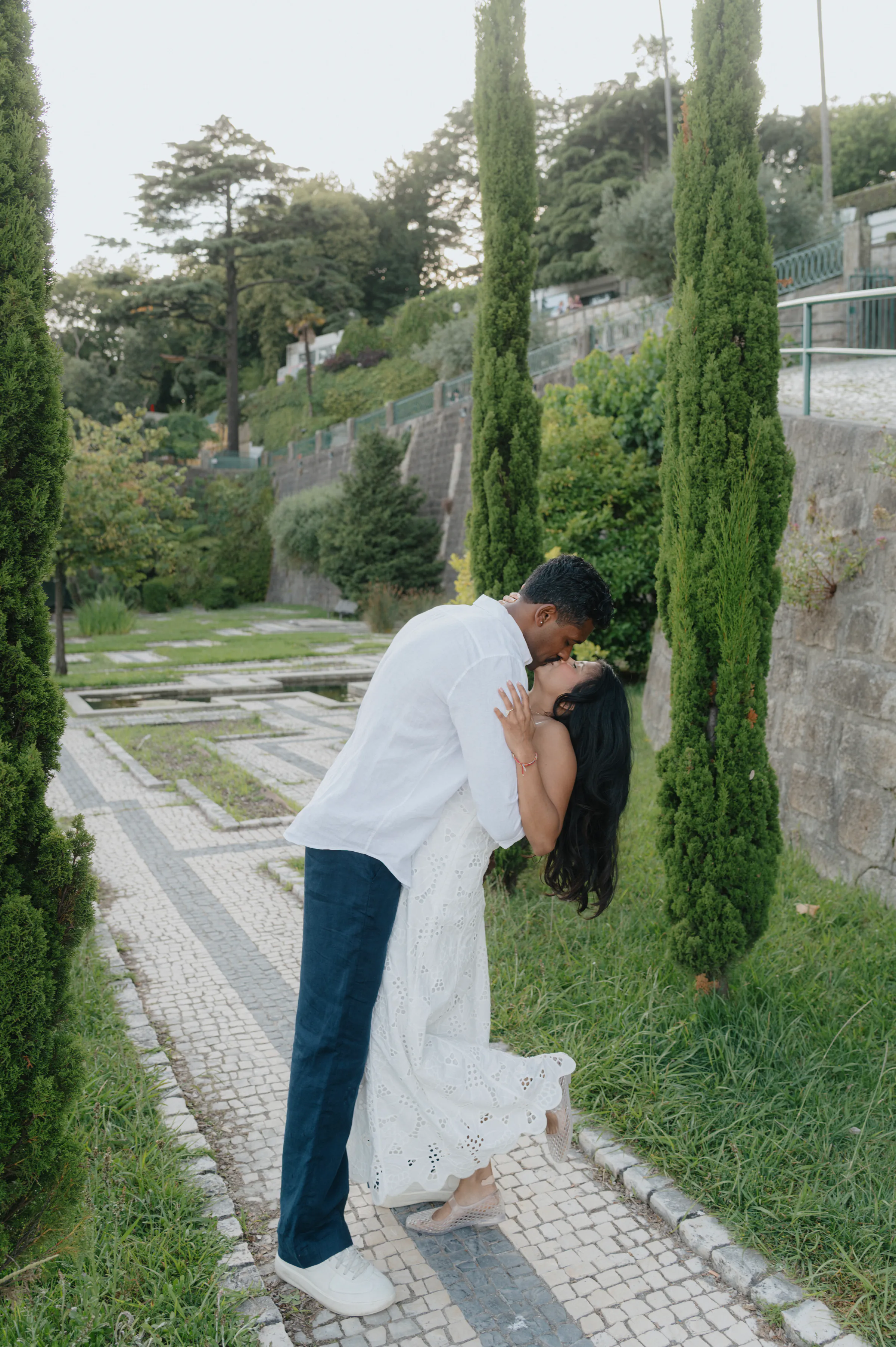 Couple kissing on a garden path lined with tall cypress trees during an outdoor session.