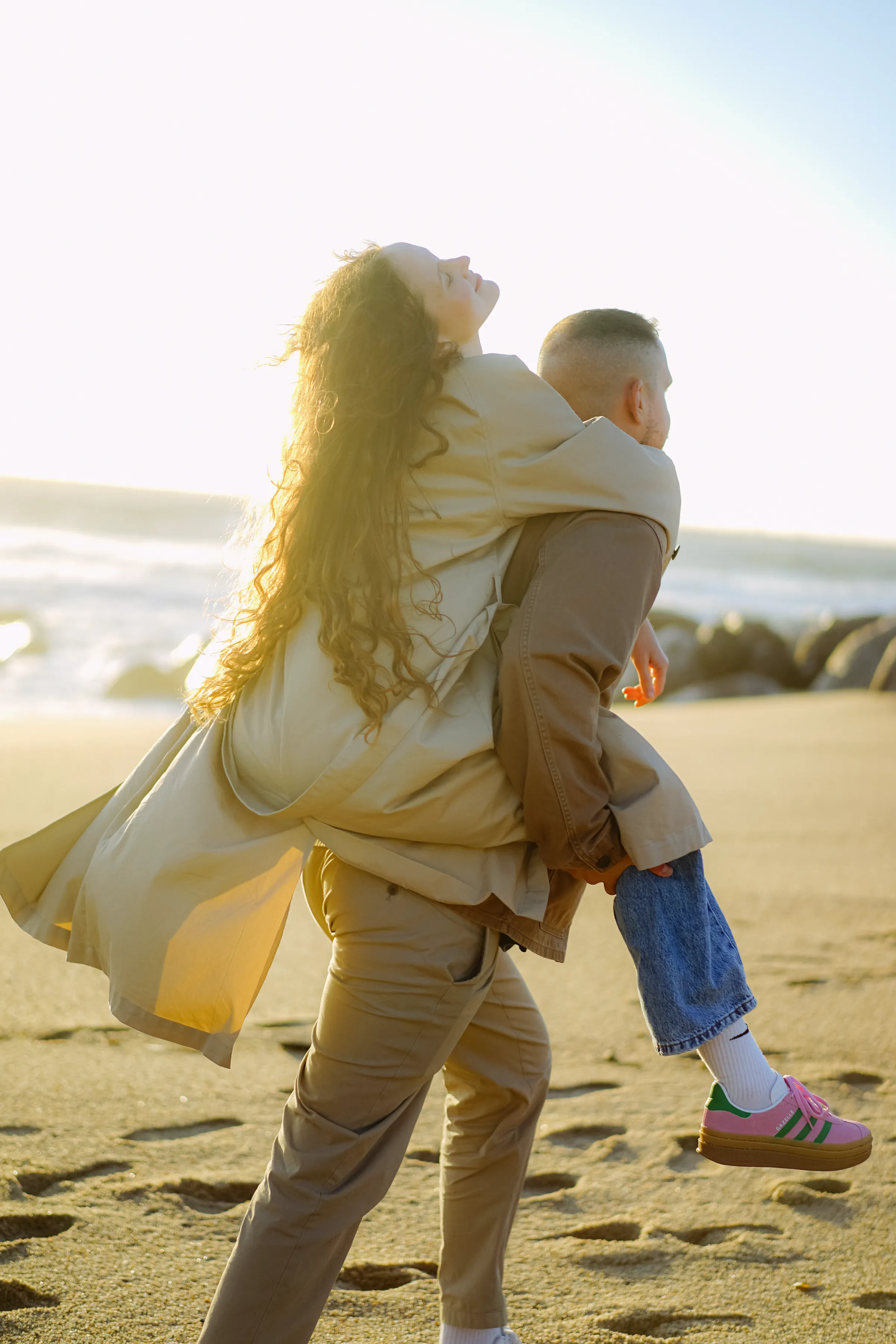 Adult carrying a child during a soft light seaside session on a sandy beach.