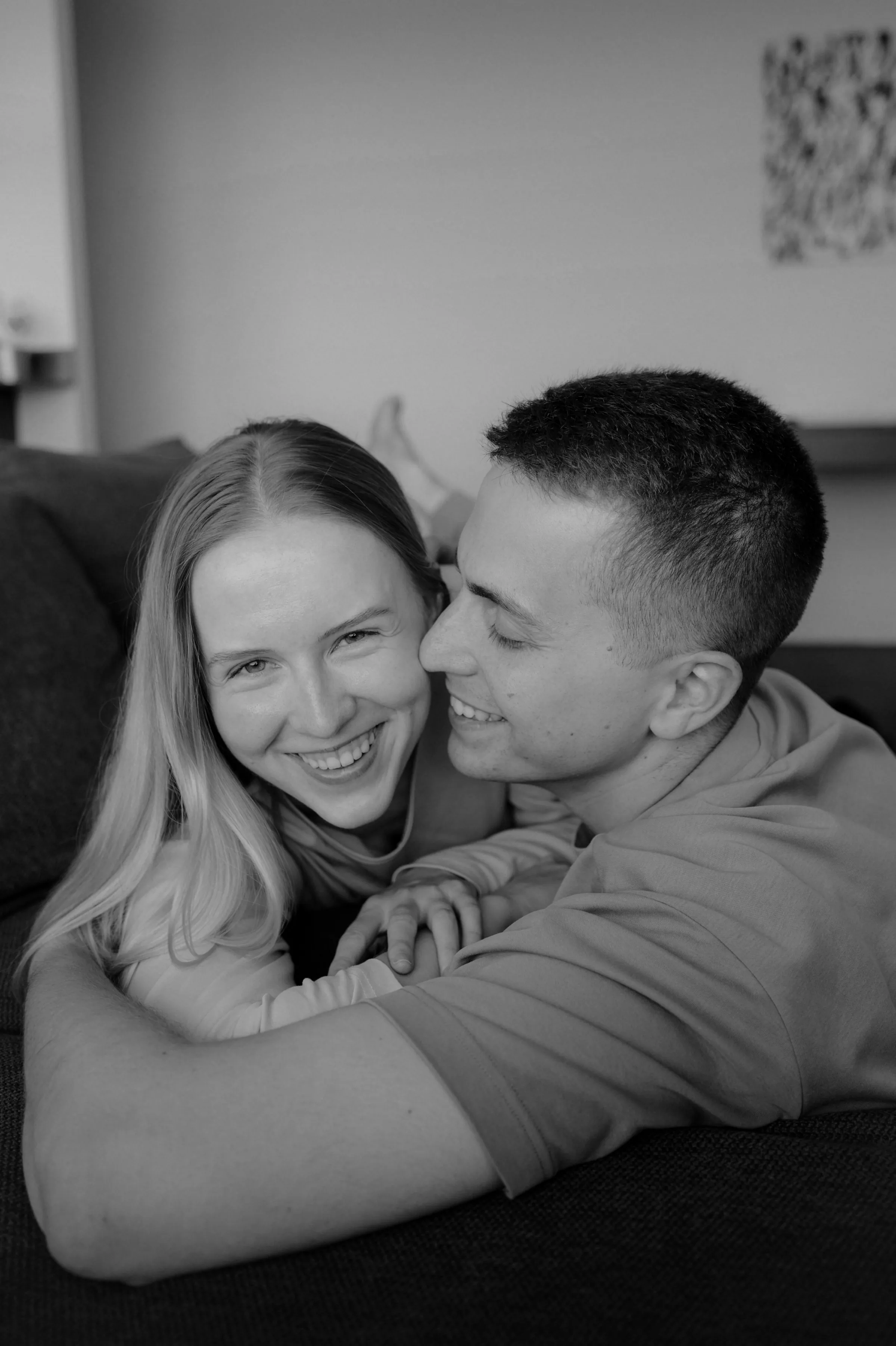 Black-and-white close portrait of a couple cuddling on a couch during an indoor session.