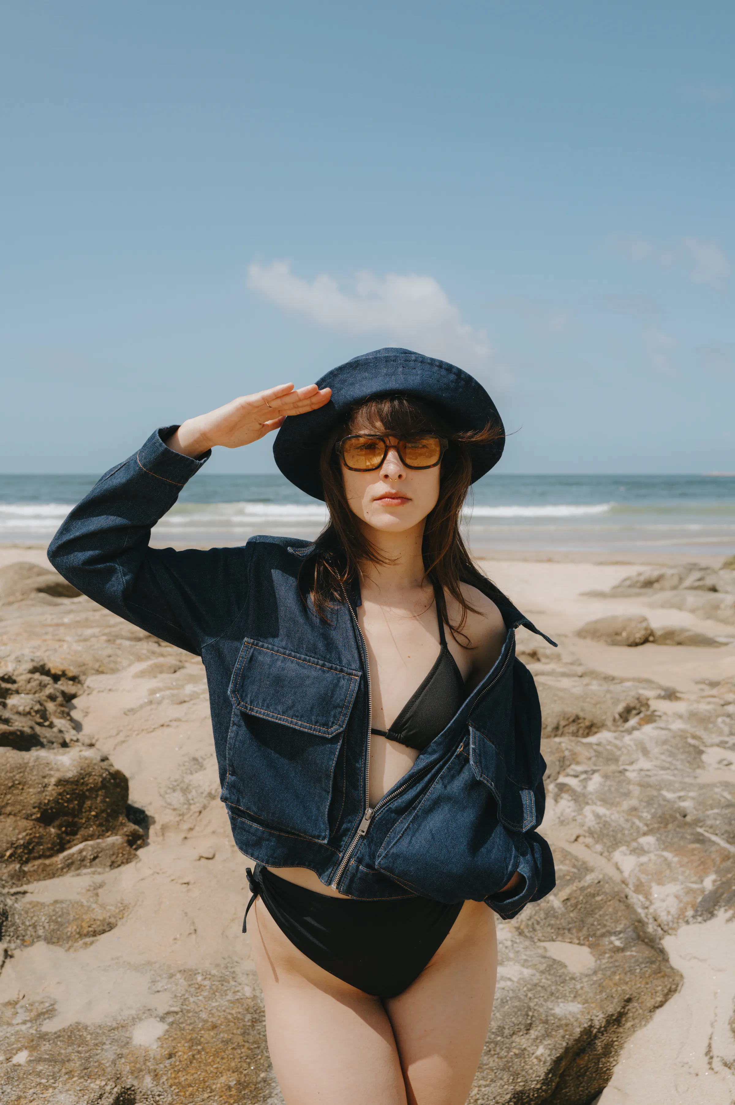 Seaside portrait of a person in sunhat and sunglasses standing on rocks by the shore