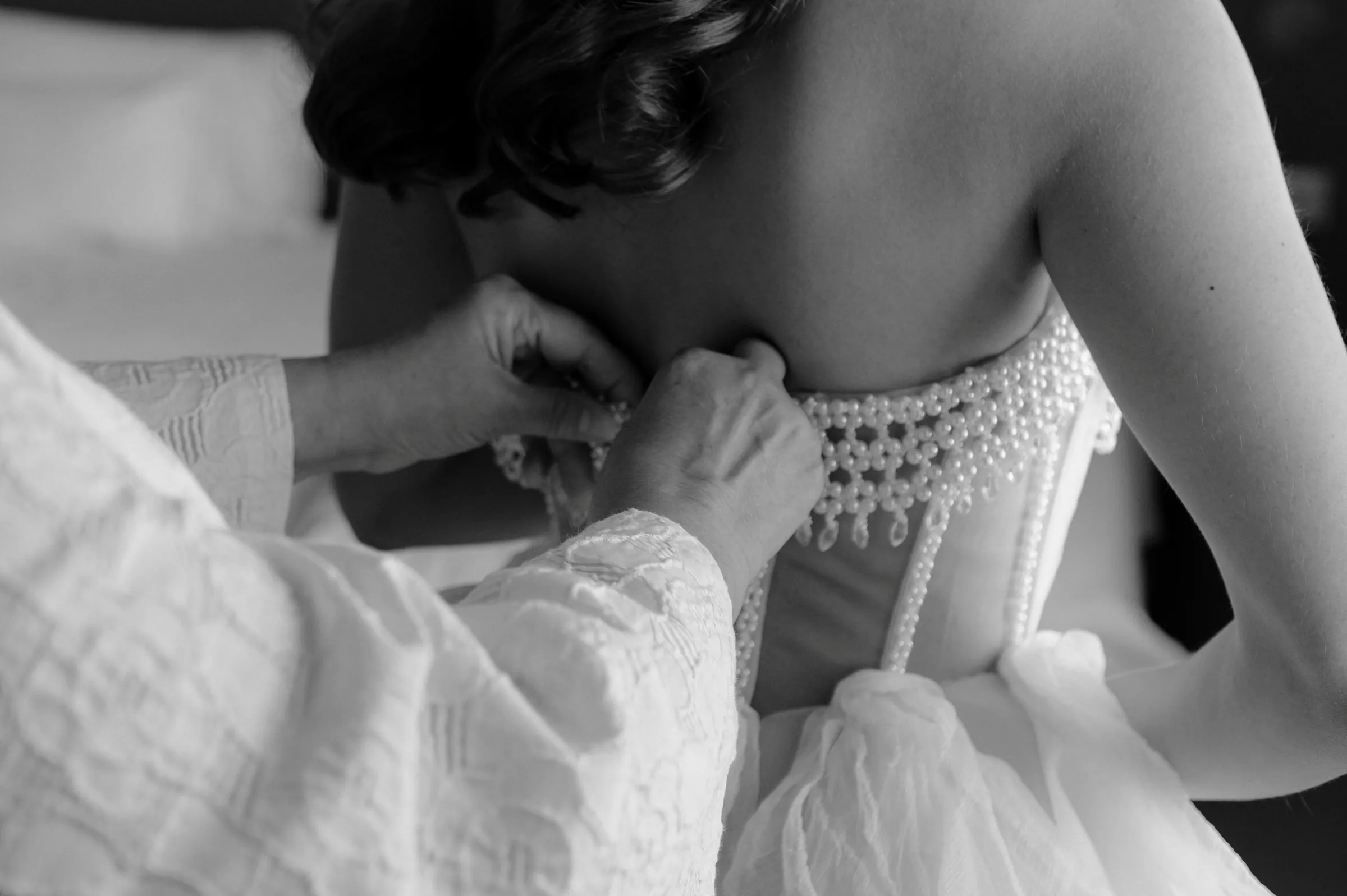 Close detail of hands fastening a beaded dress during an indoor getting-ready session.