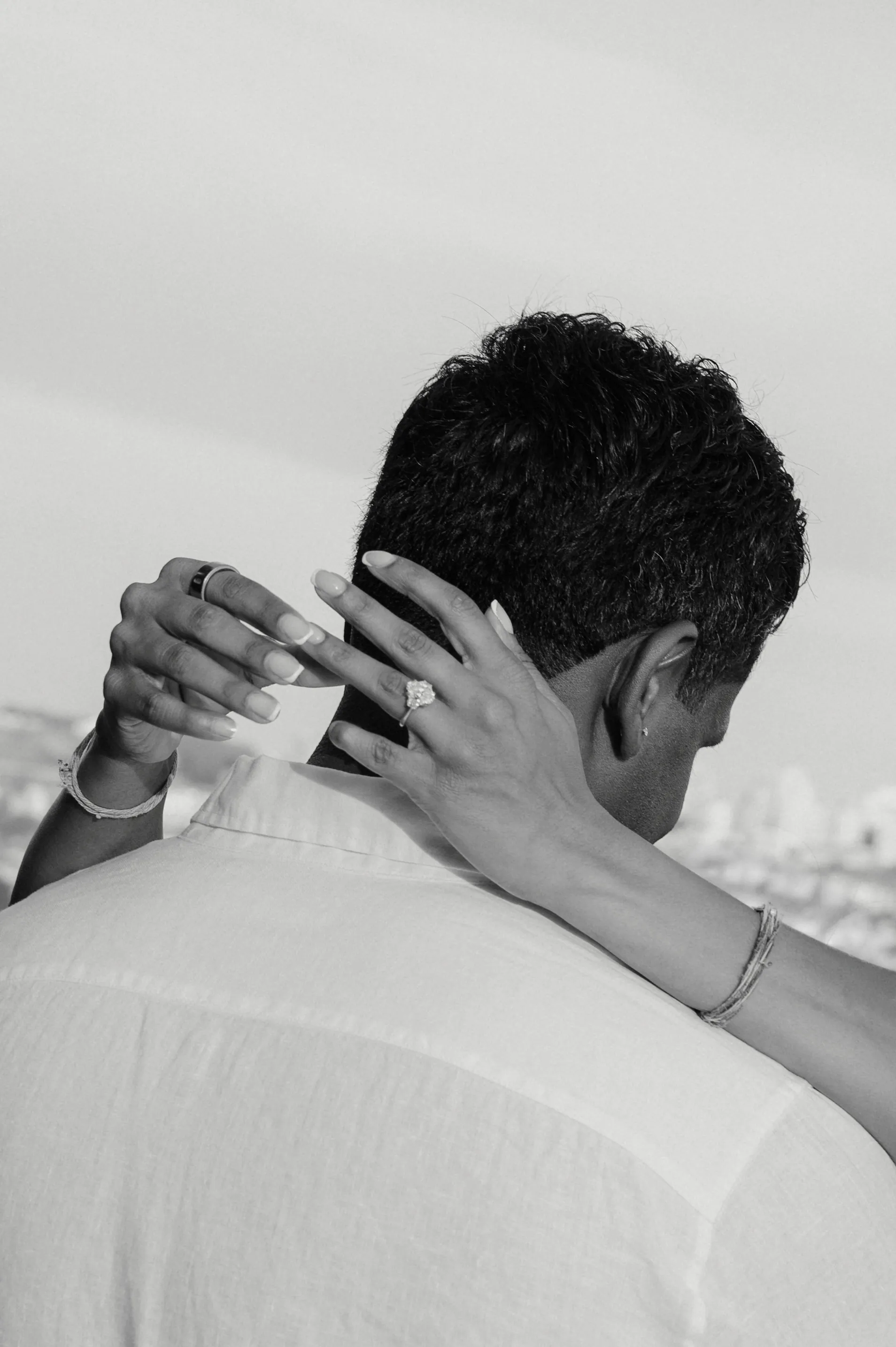 Black-and-white close portrait of a couple embracing from behind in soft outdoor light.