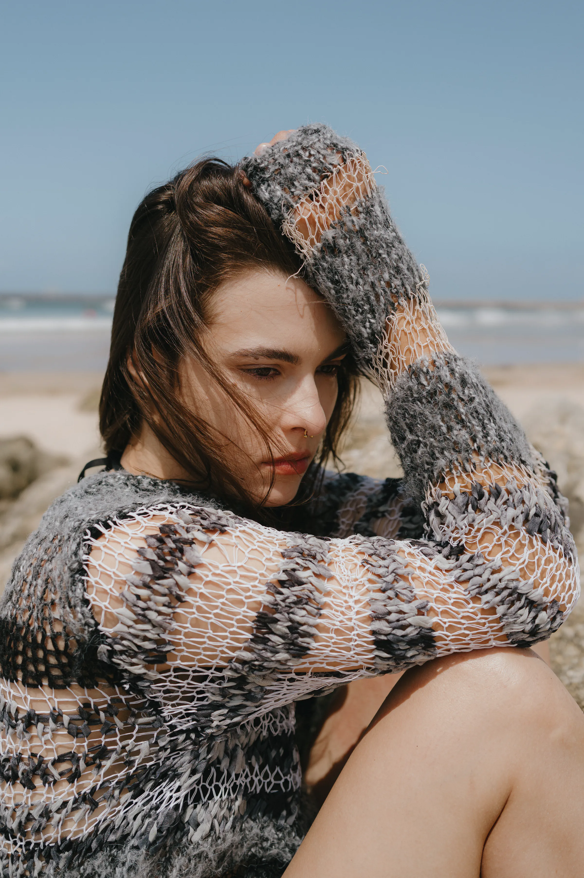 Close portrait of a woman seated on the beach in a textured knit sweater, with soft coastal light.