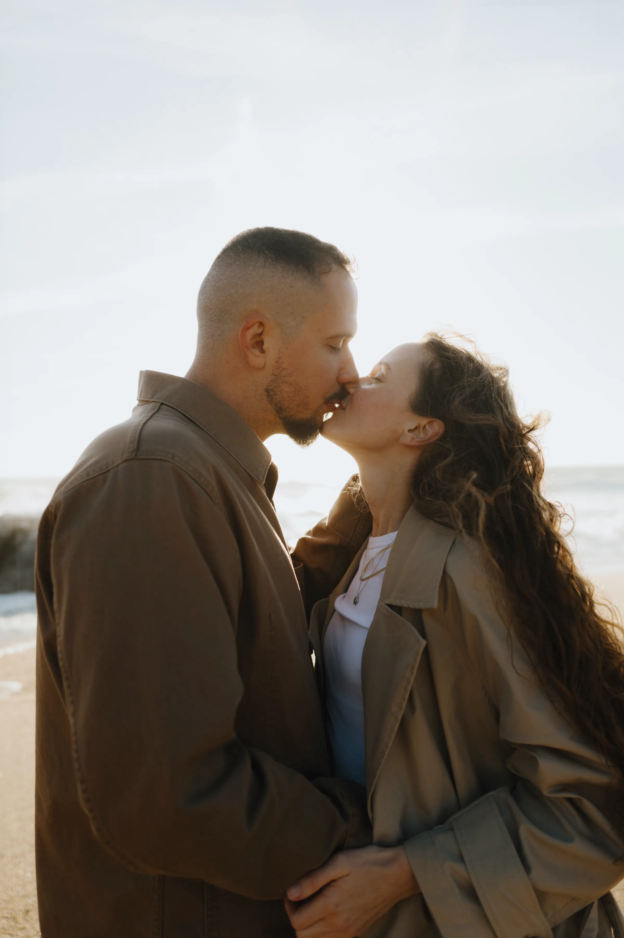 Couple kissing during a seaside outdoor session in soft natural light.