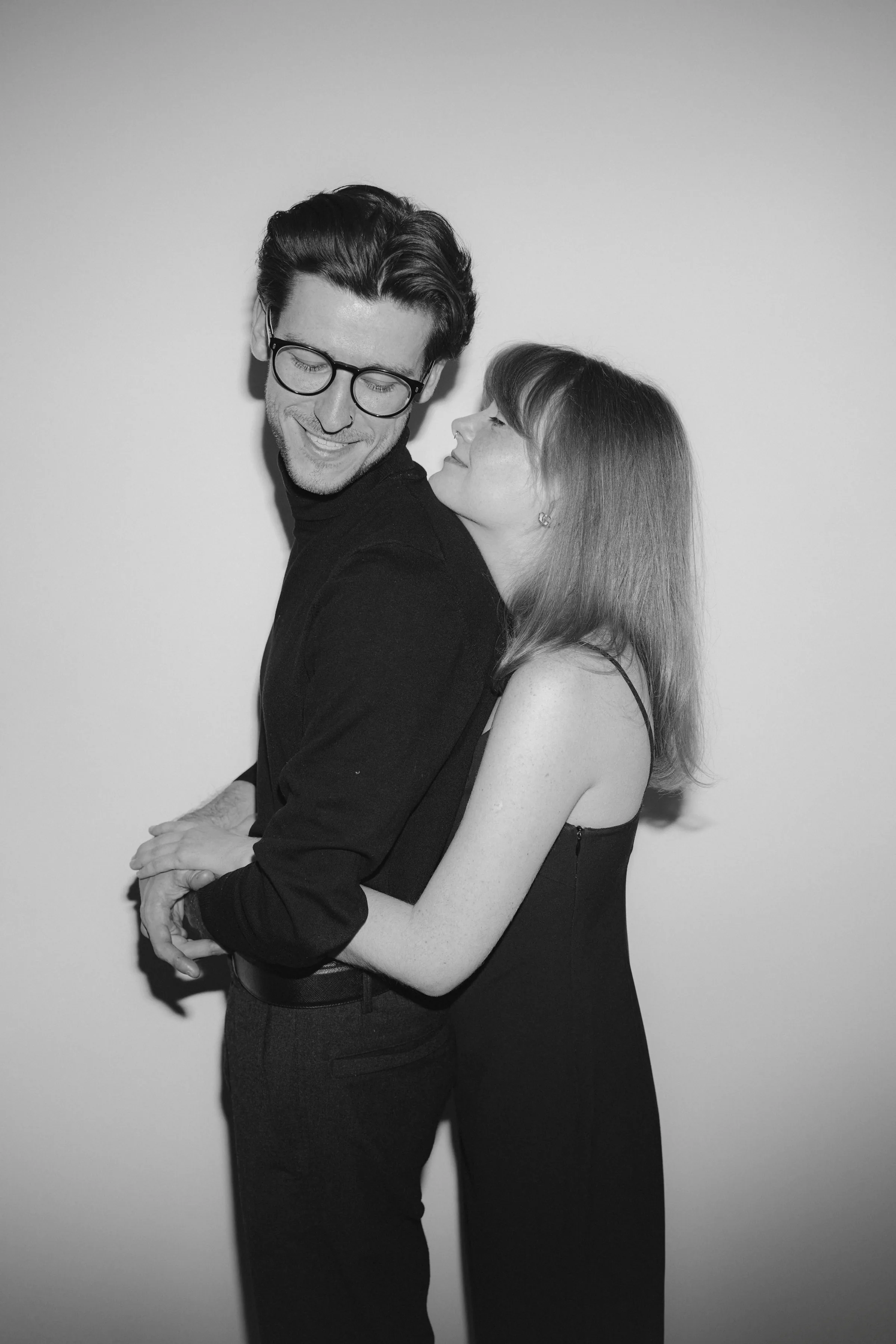 Black-and-white close portrait of a couple embracing against a plain studio wall.