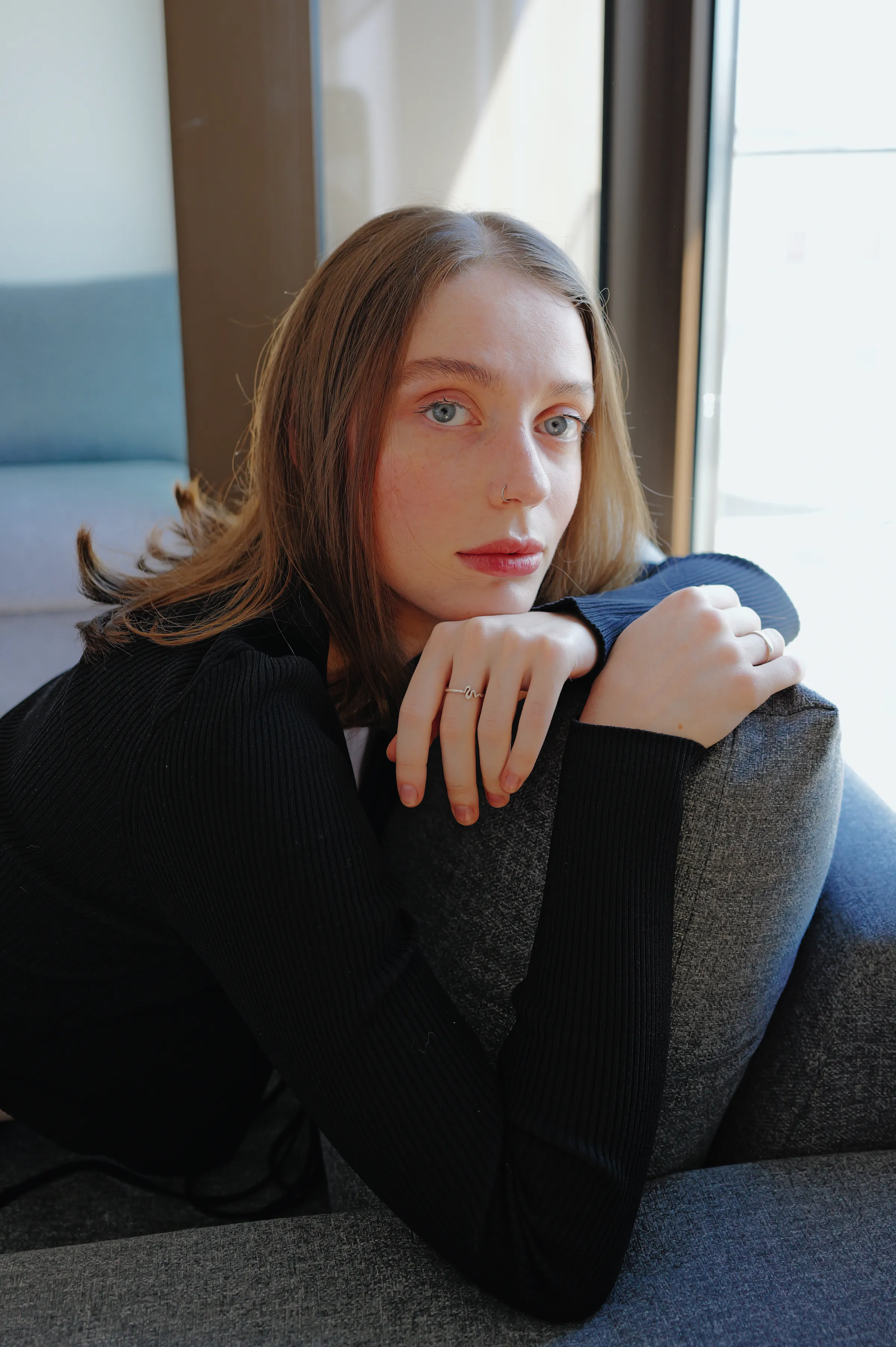 Close portrait of a person leaning on a sofa by a window in soft light.