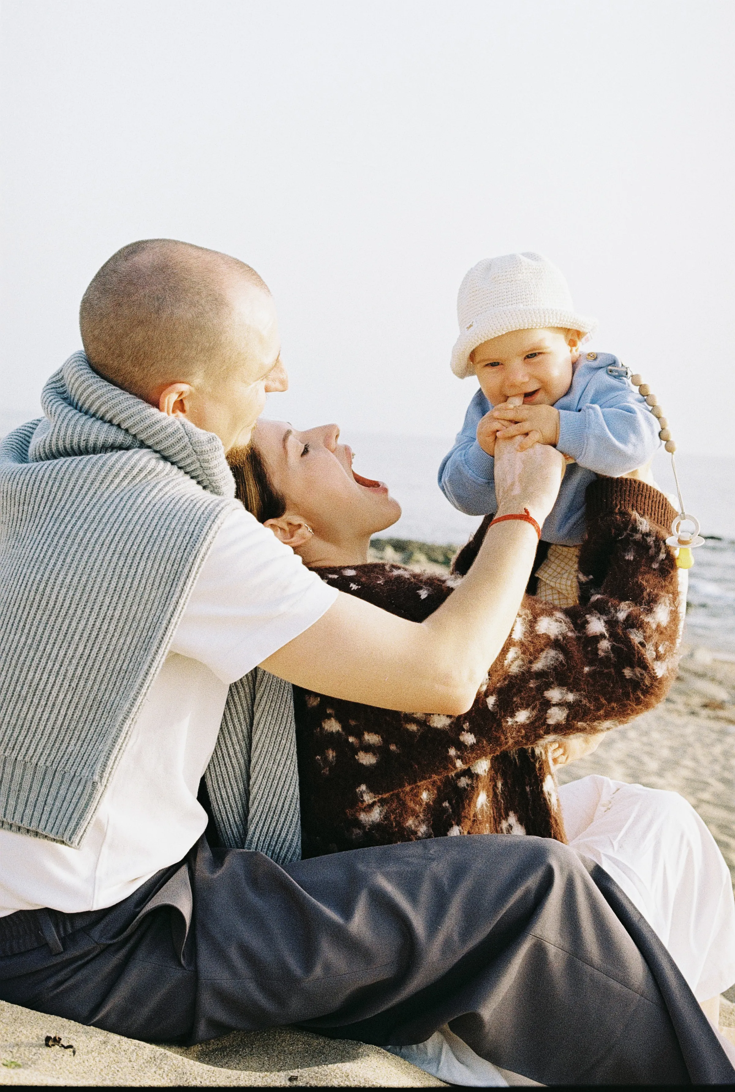 Family seaside portrait with two adults holding a baby in soft light on the sand