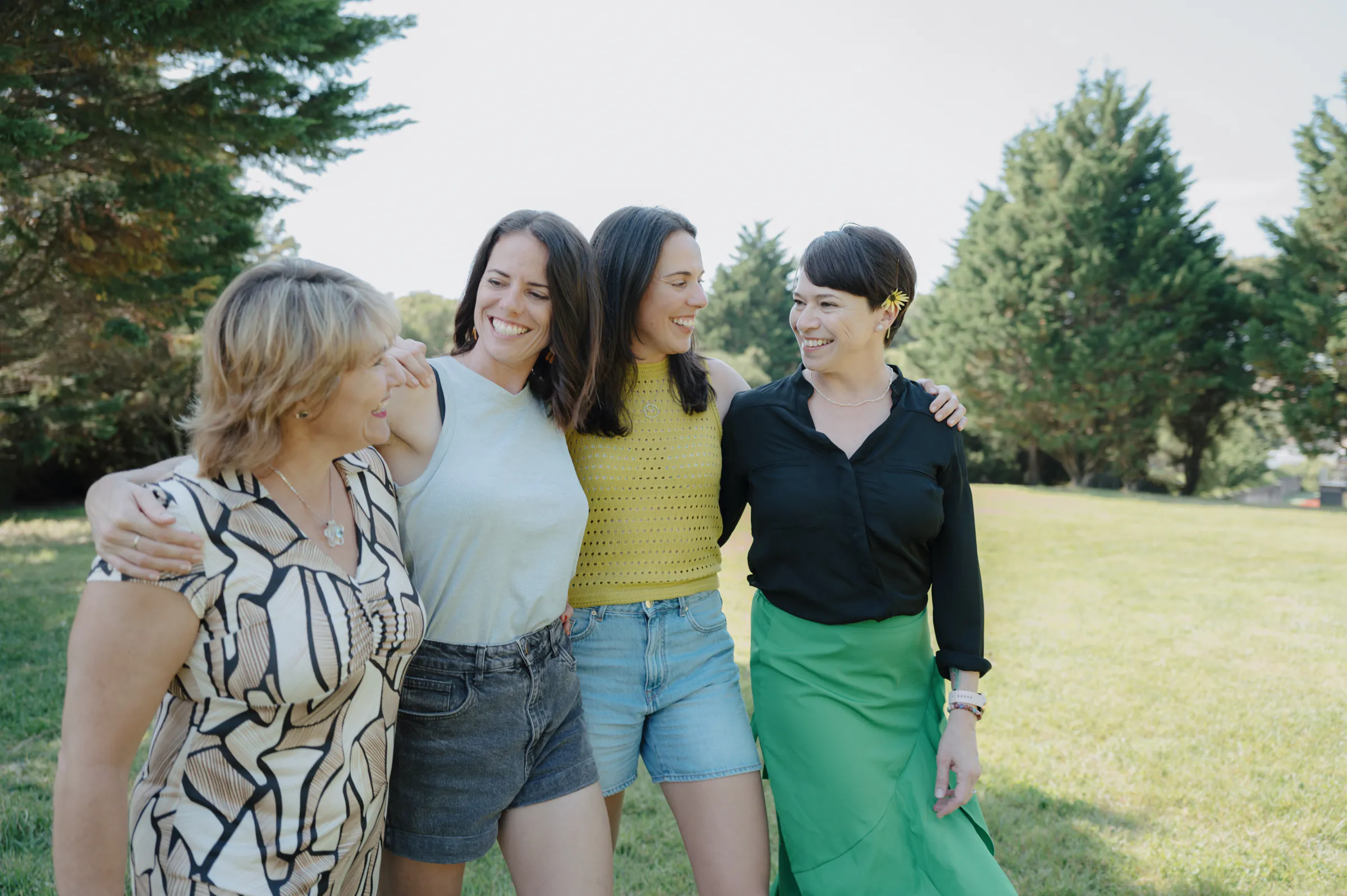 Group portrait of four adults standing arm in arm during an outdoor park session in soft light.