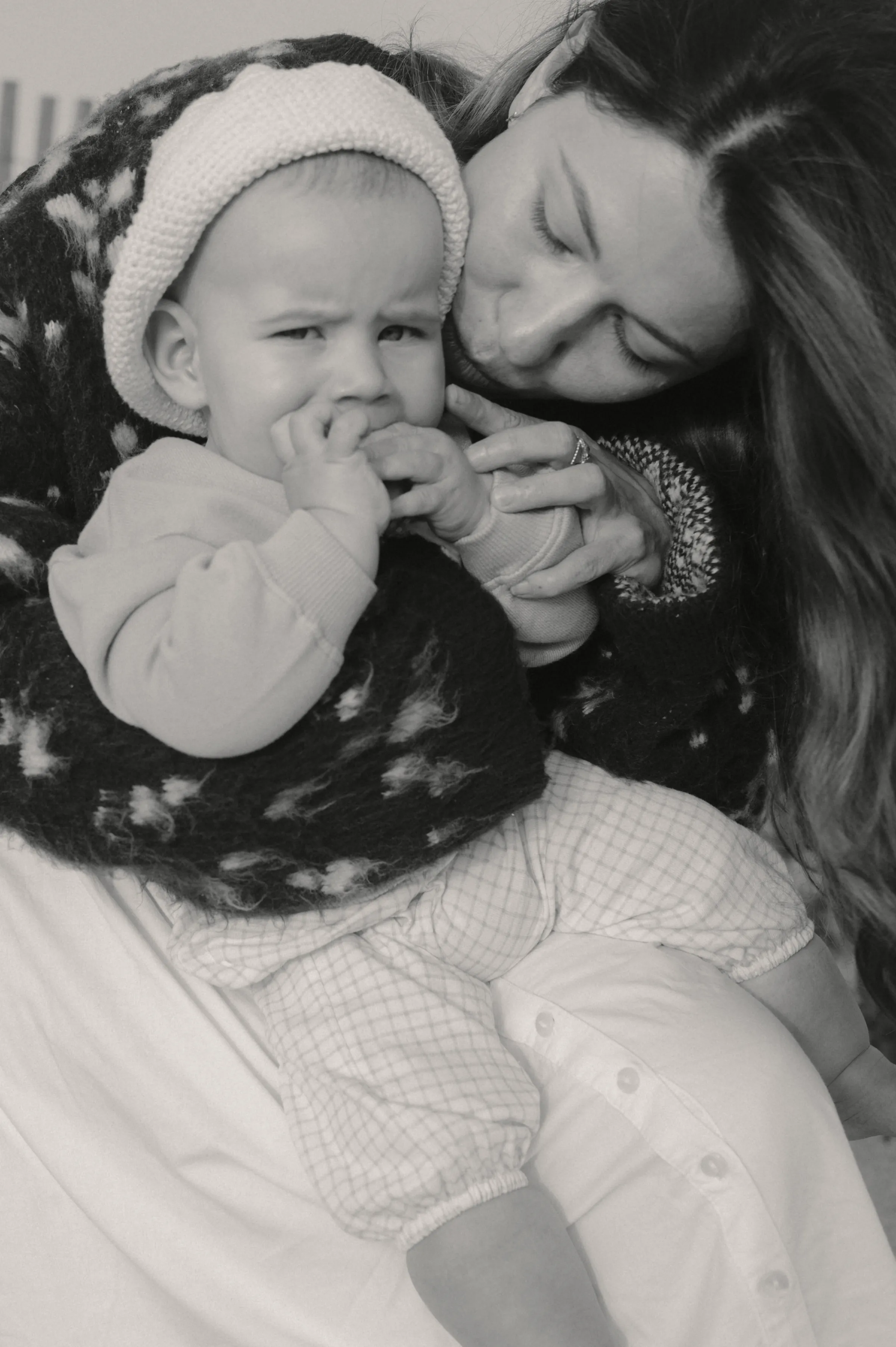 Black-and-white close portrait of an adult holding and kissing a baby in soft light.