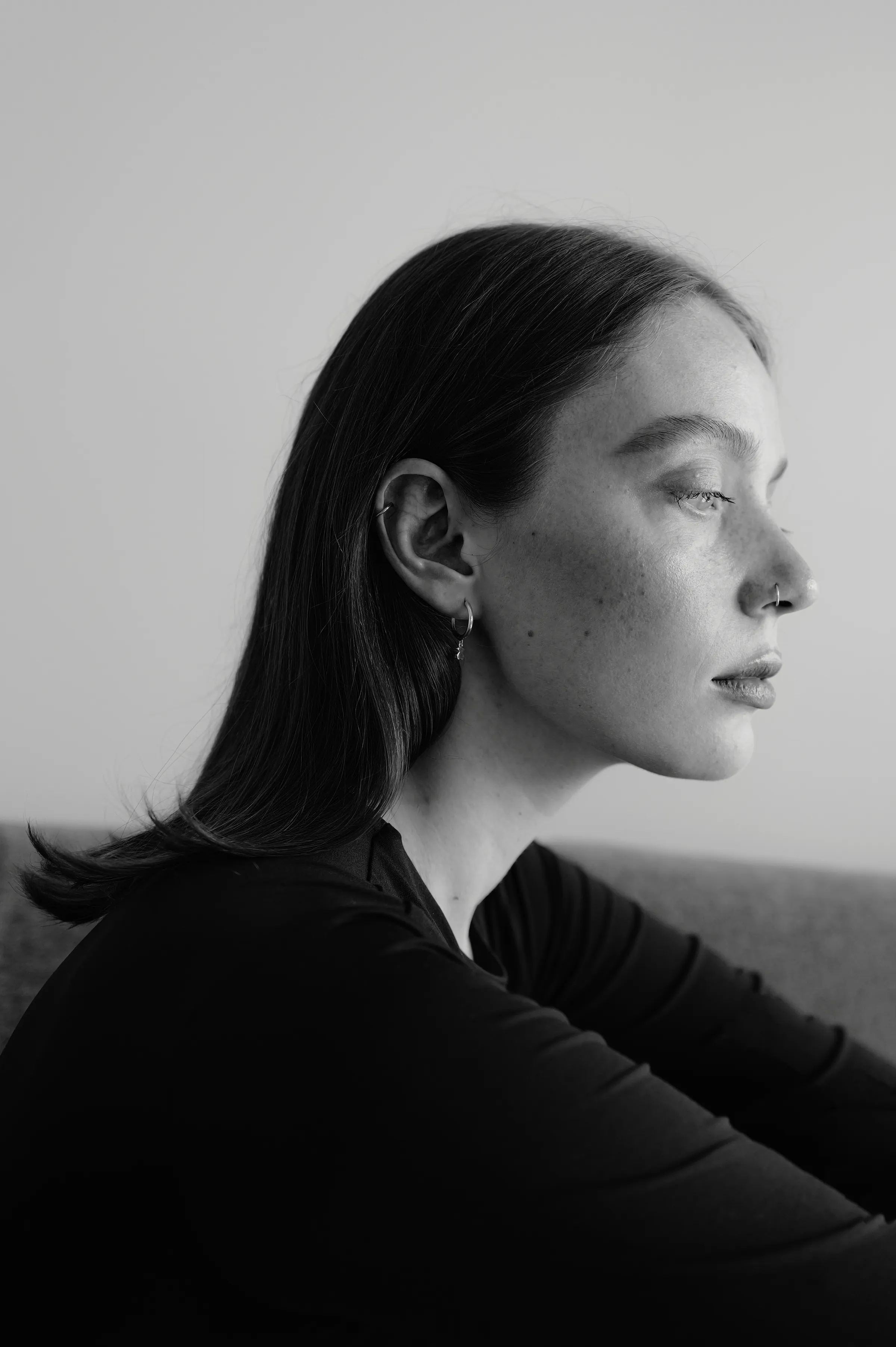 Black-and-white close portrait of an adult in side profile, seated indoors against a plain wall.