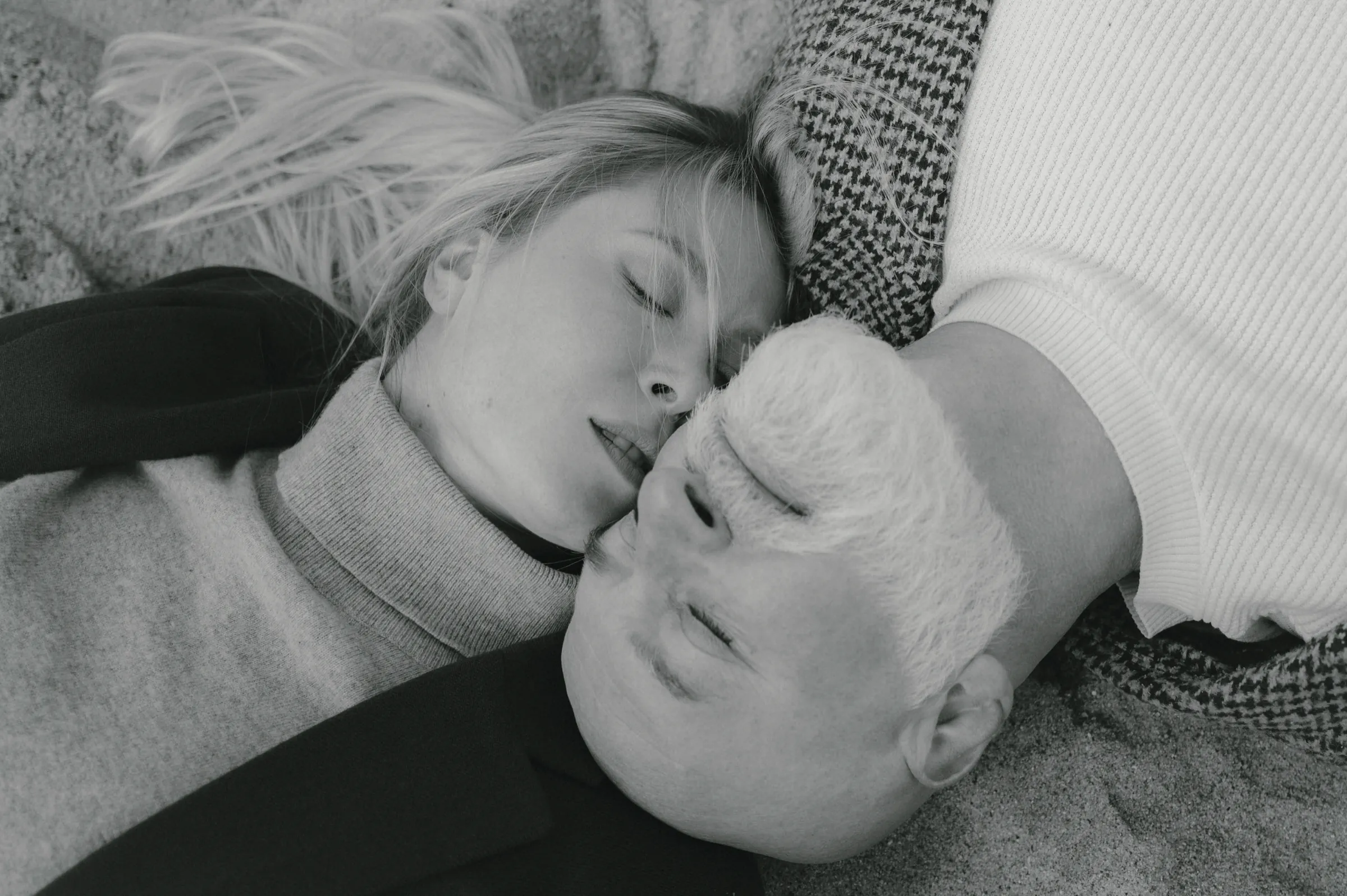 Black-and-white close portrait of a couple lying close together, heads touching in a quiet indoor frame.