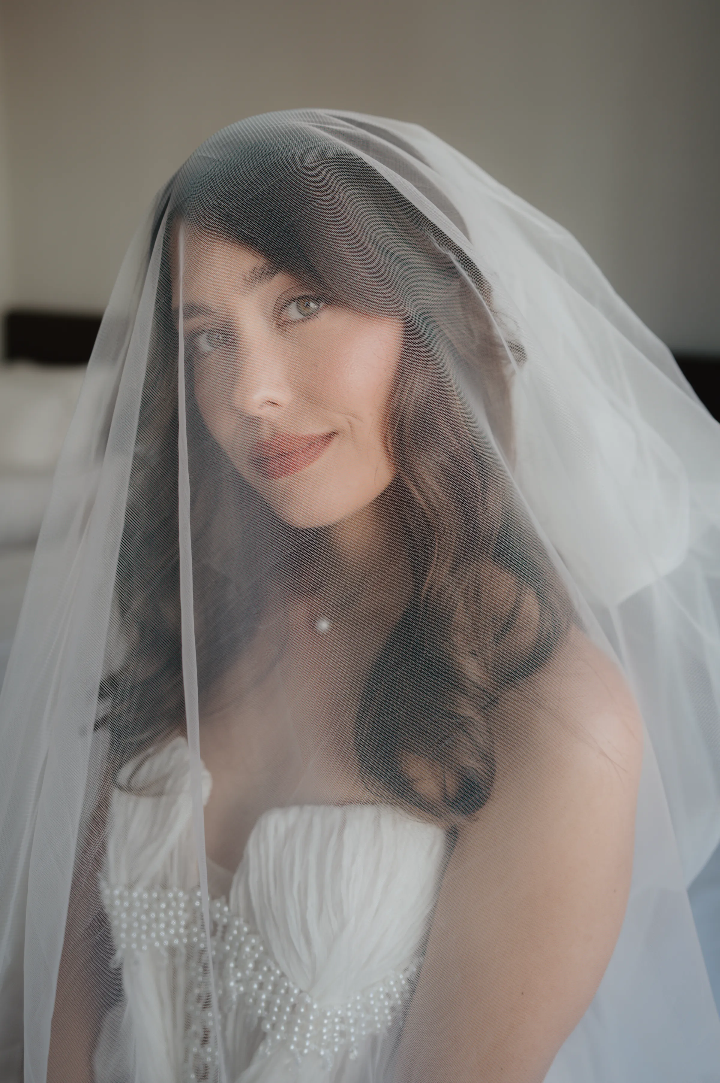 Close portrait of a bride under a sheer veil, wearing a strapless gown in soft indoor light.