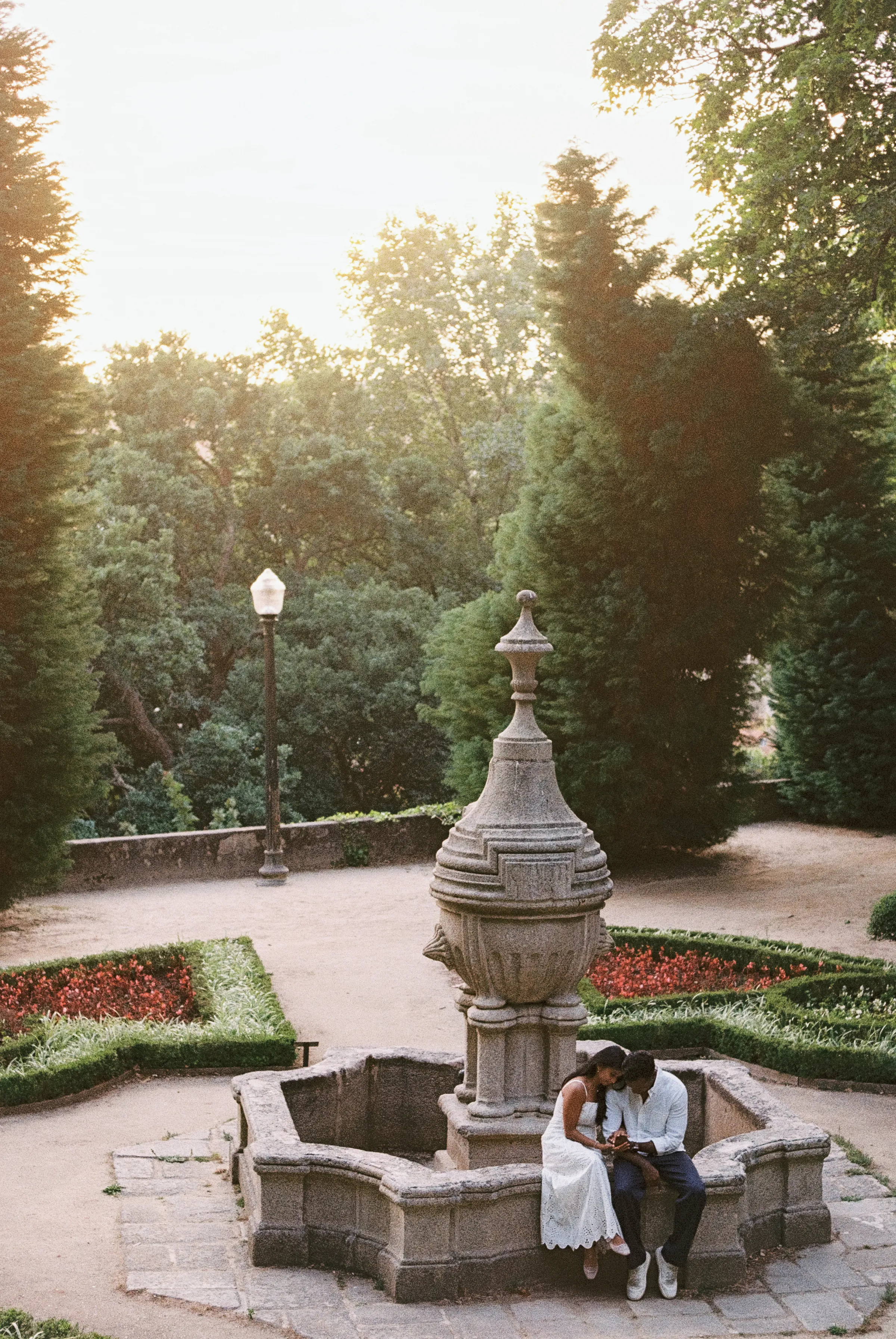 Couple seated by a stone fountain during a soft light garden portrait session.