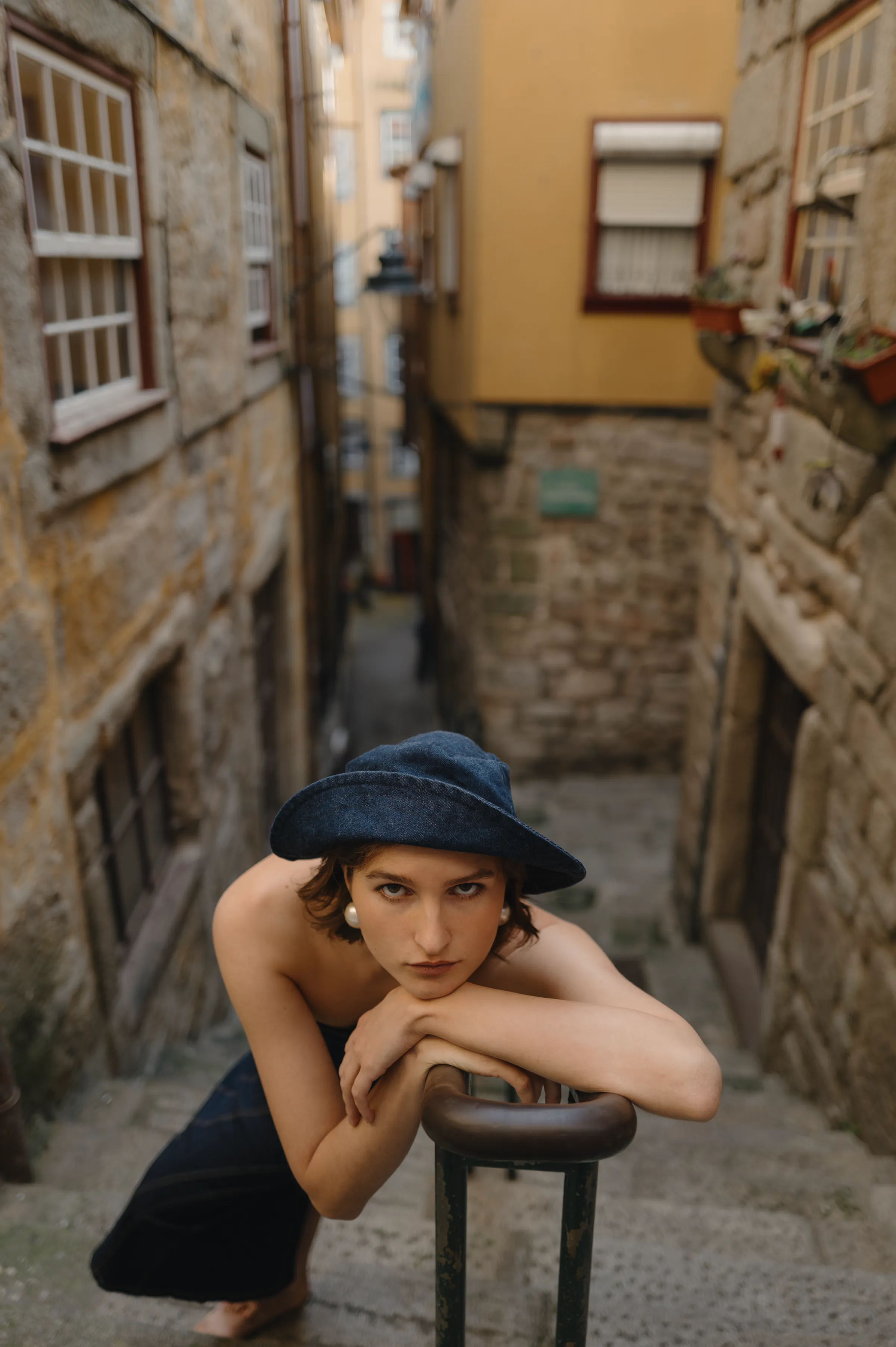 Outdoor portrait of a person in a dark hat leaning on a railing along narrow stone city steps.