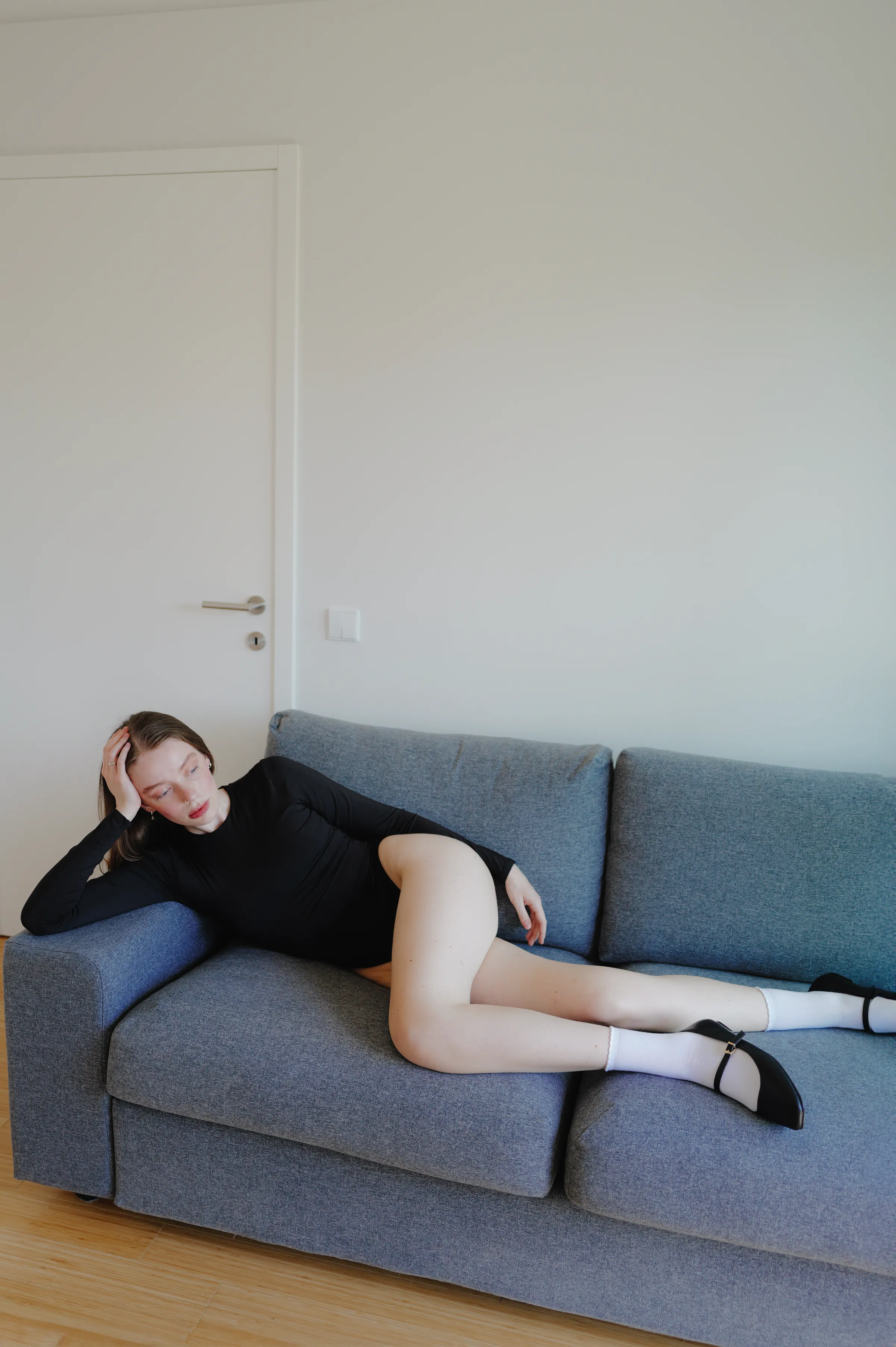 Home session portrait of an adult reclining on a gray sofa in soft light.
