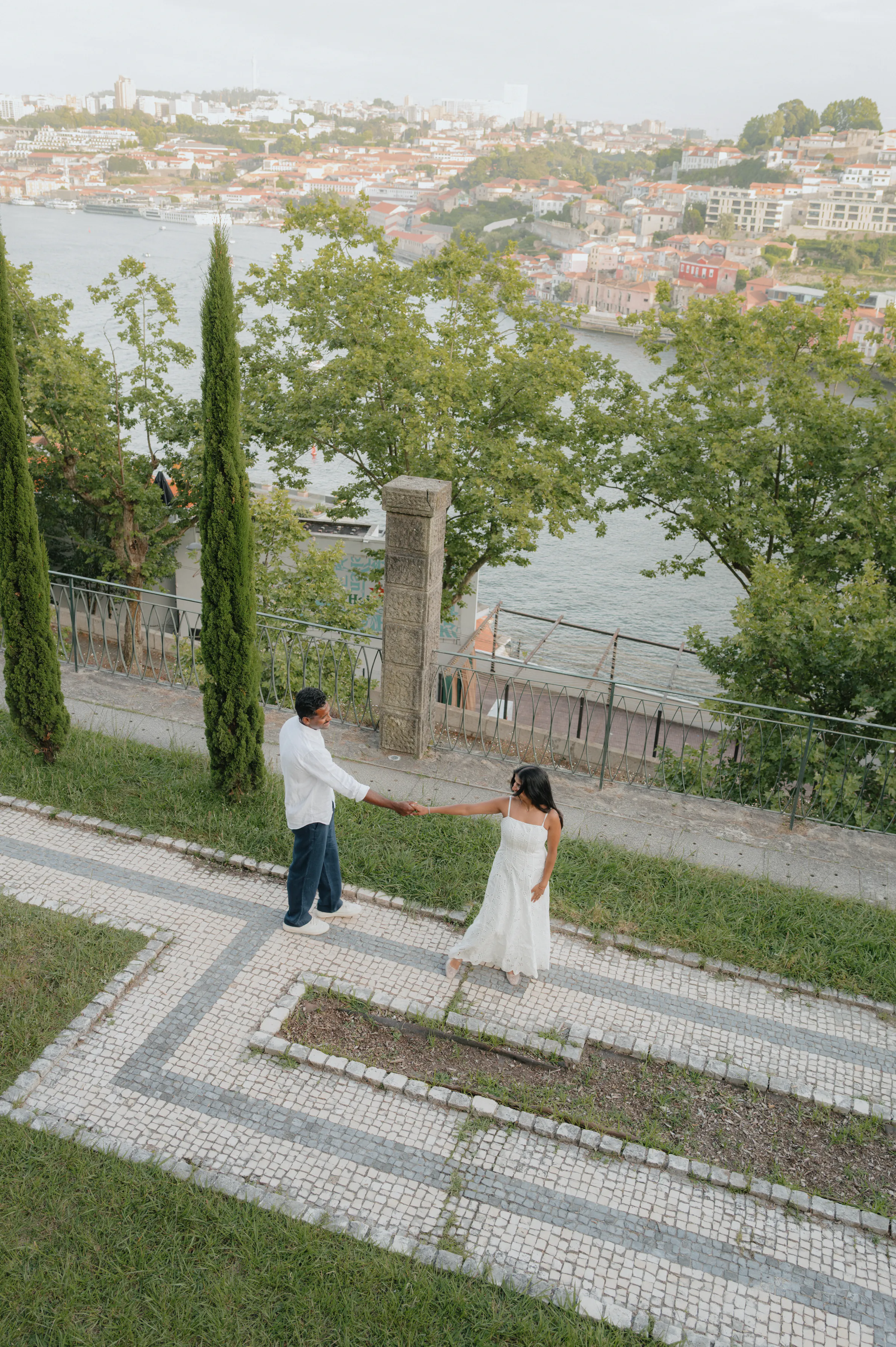 Couple on a hillside path during a city walk, overlooking a river in soft light.