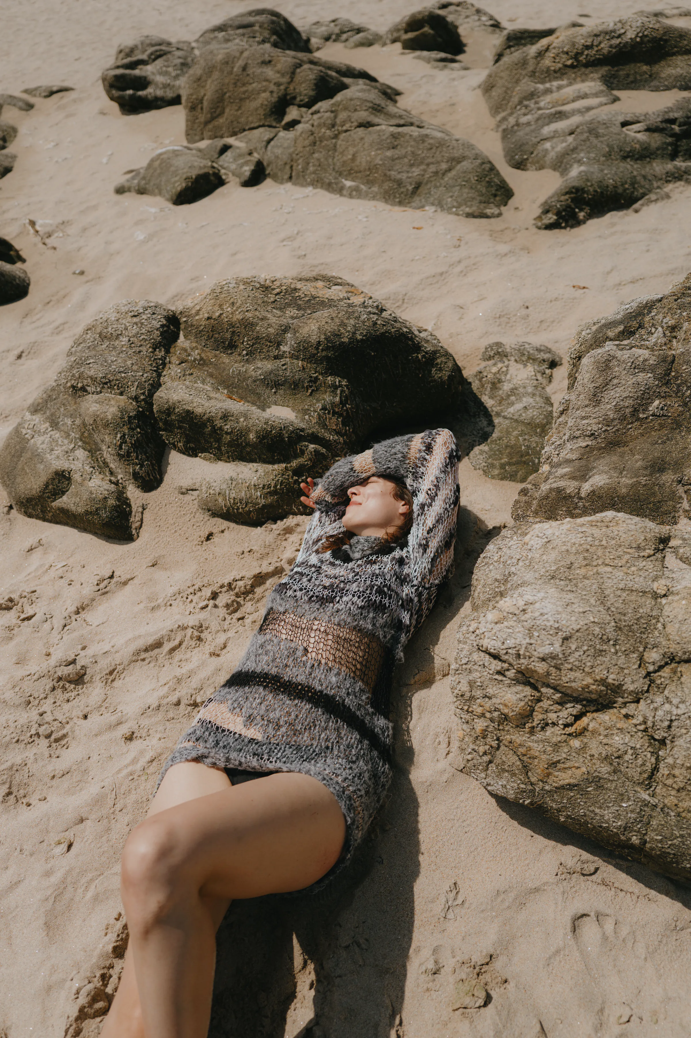 Seaside portrait of a person reclining on sandy rocks in soft sunlight.