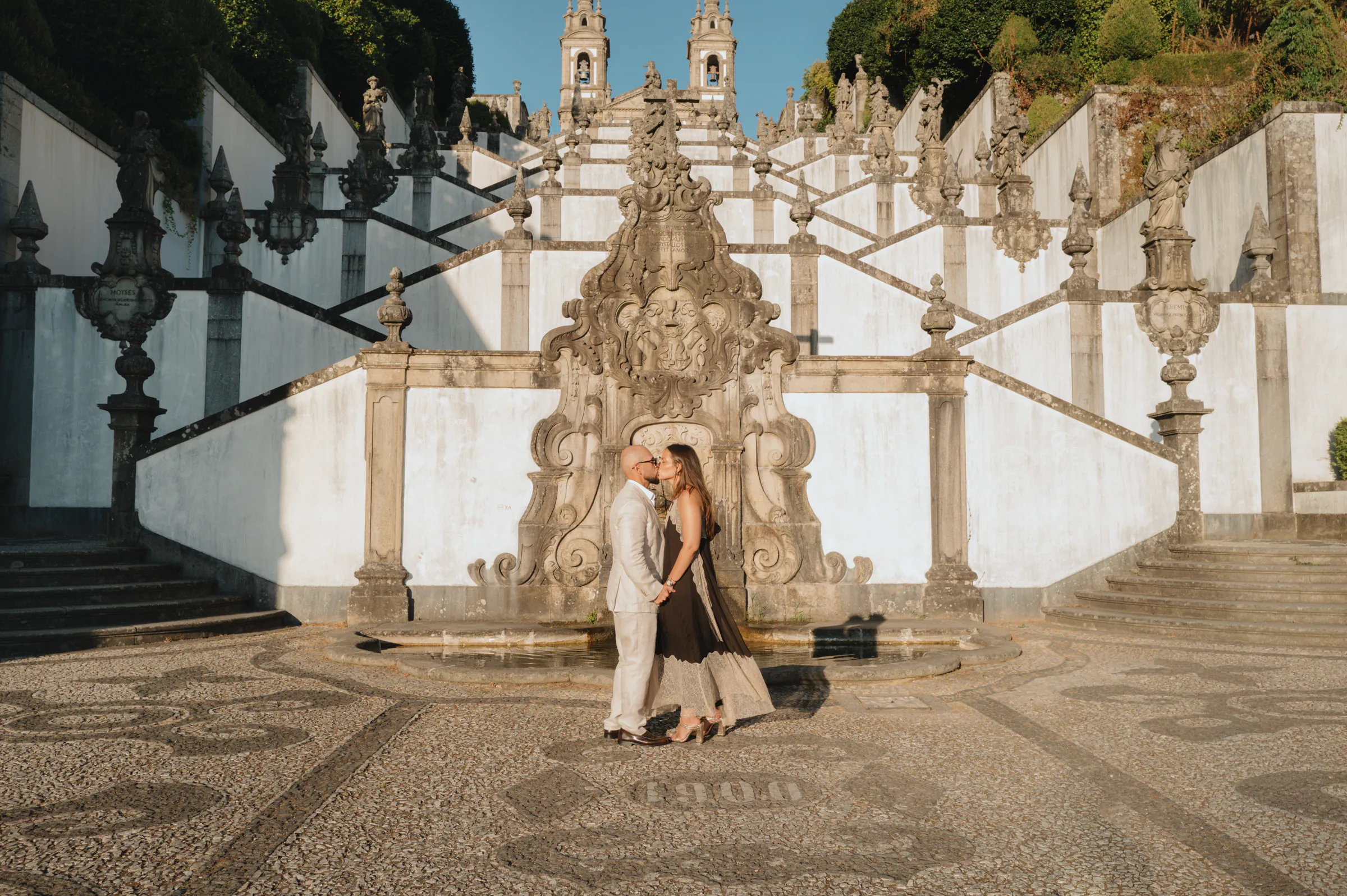 Couple portrait in soft light before ornate stone stairs and a fountain during a city walk.