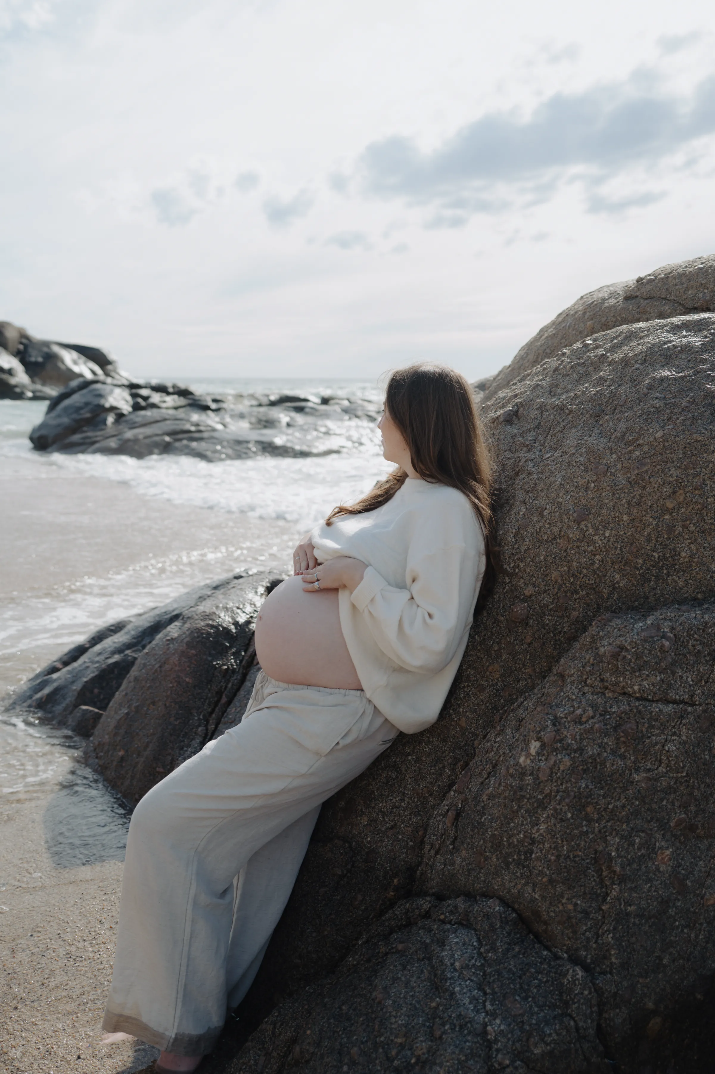 Seaside portrait of a person in cream clothing leaning against rocks by the waves