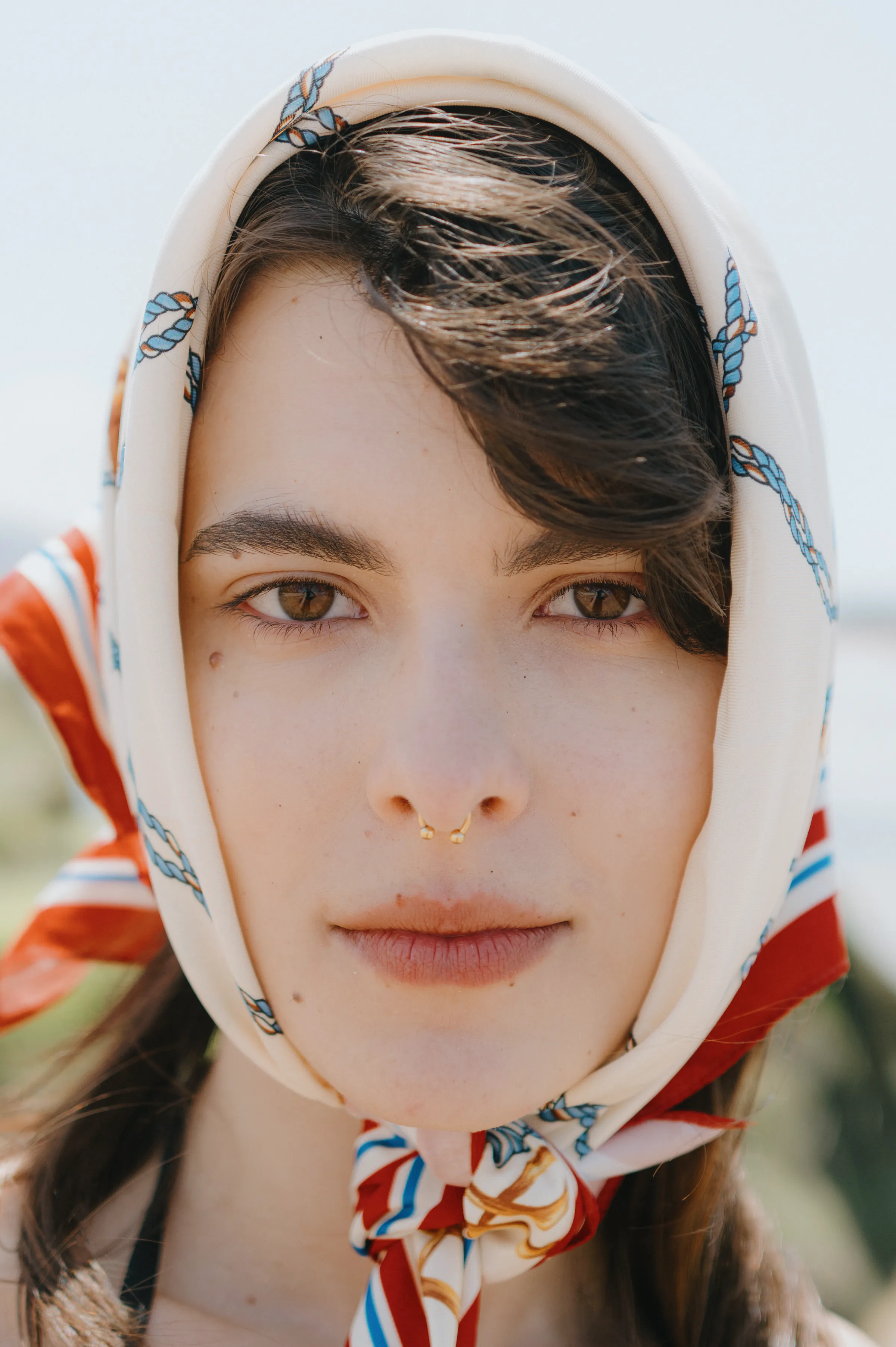 Close portrait of a person in a patterned headscarf outdoors, with soft light and blurred greenery.