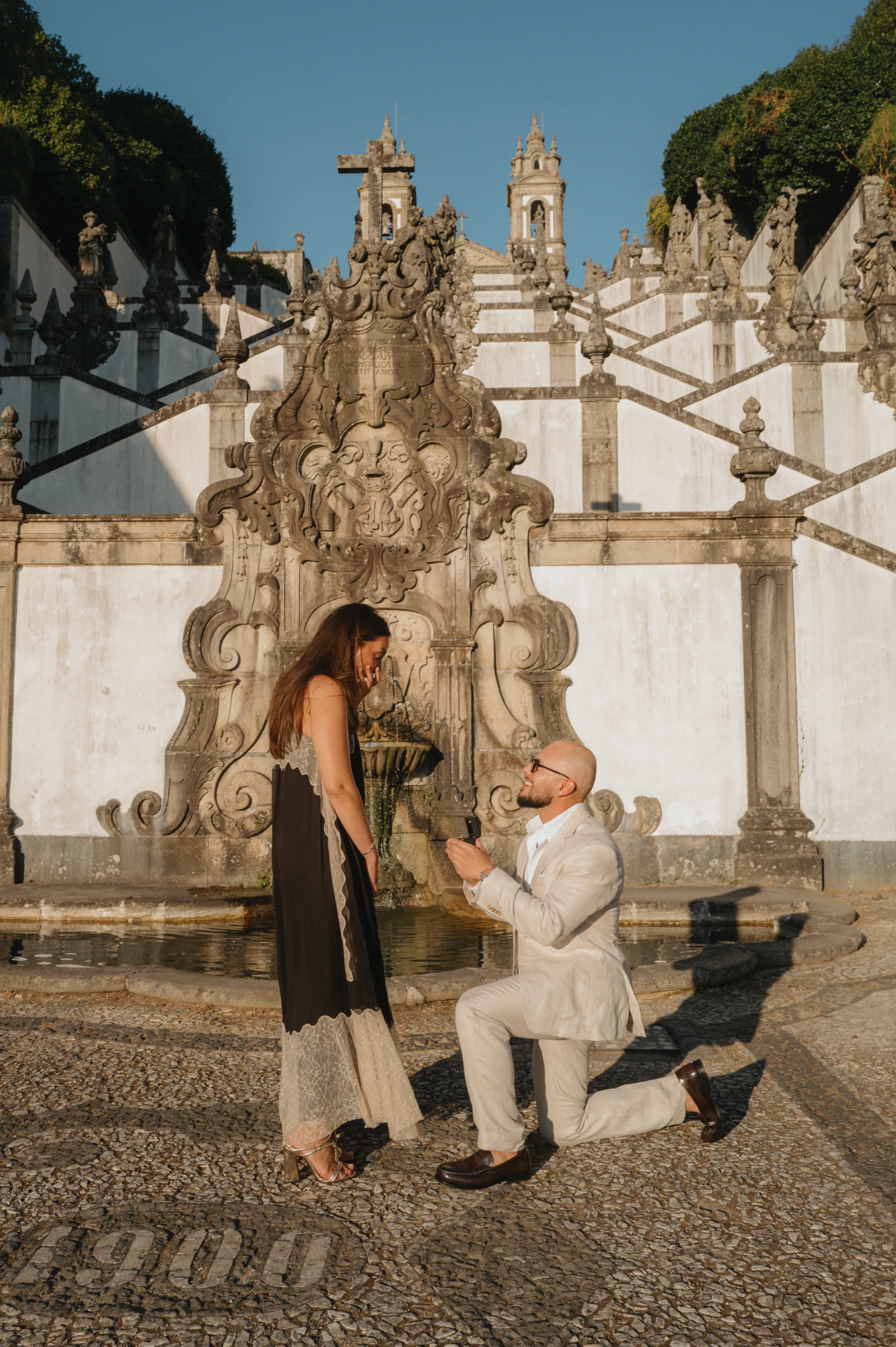 Couple during an outdoor session at an ornate staircase, one person kneeling in a proposal-like moment.