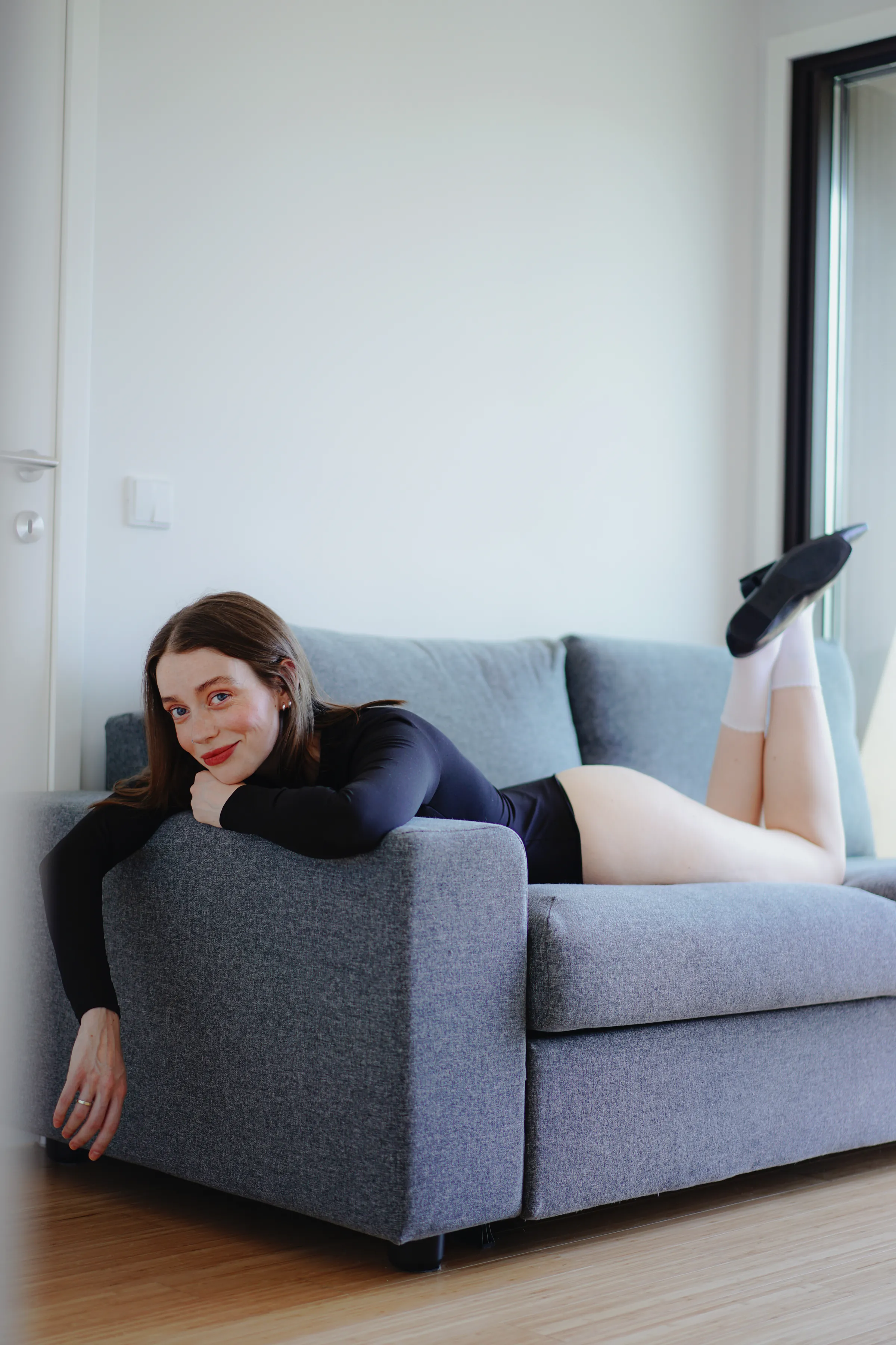 Indoor portrait of an adult reclining on a gray sofa in soft window light.