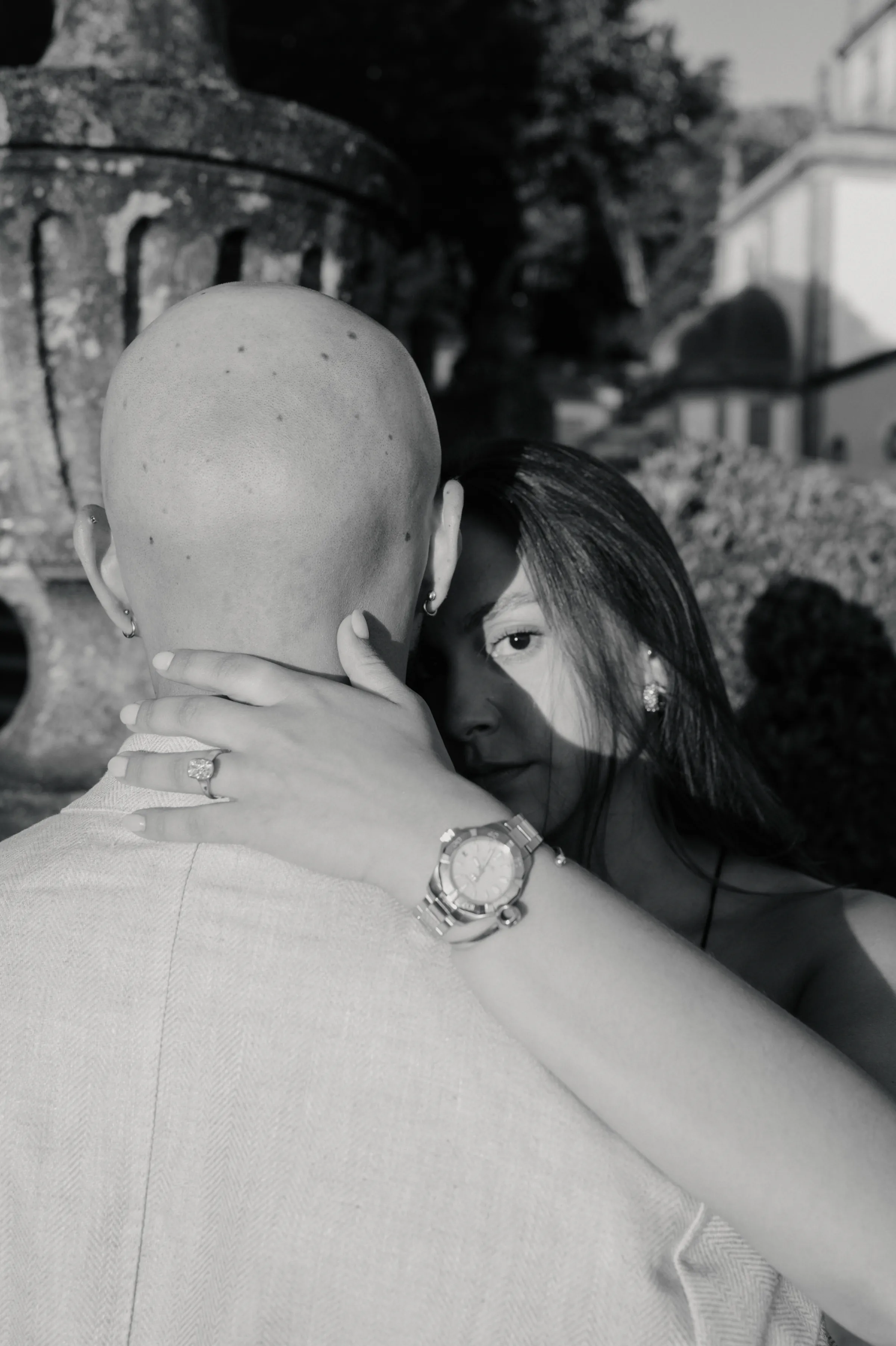 Close portrait of a couple embracing outdoors in soft light, with garden architecture behind them