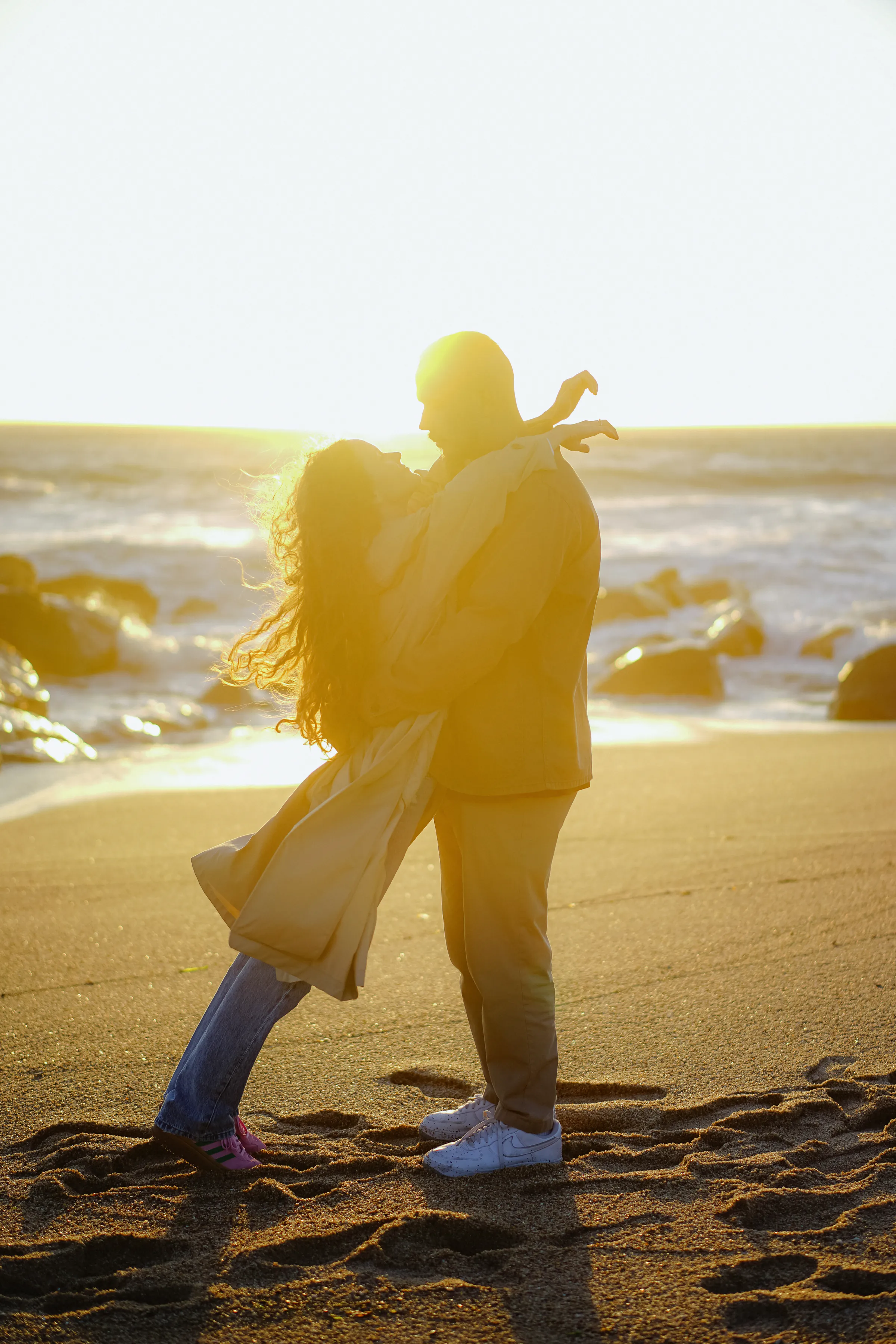 Couple embracing on a sandy seaside during a soft light outdoor session.