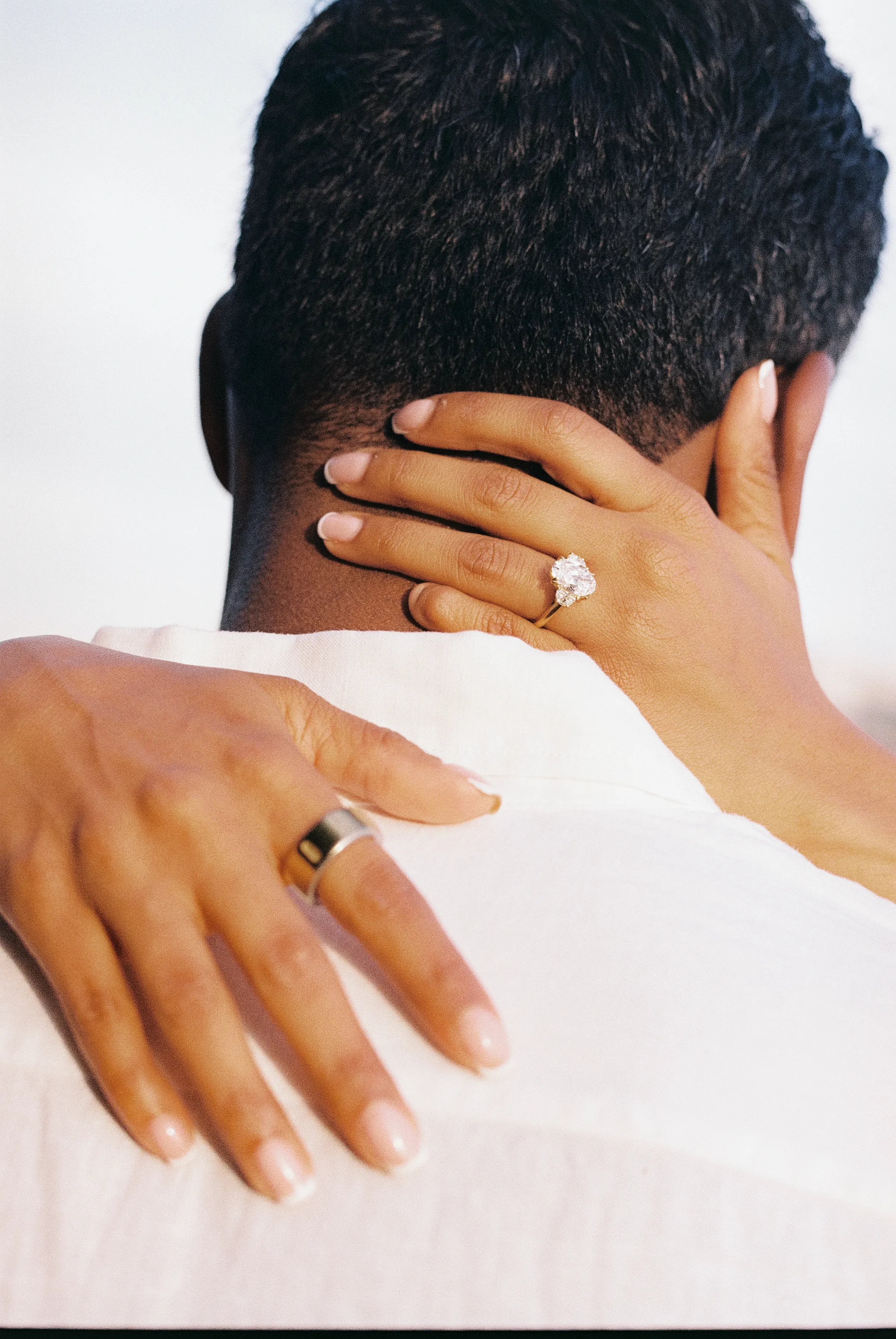 Couple close portrait with hands resting on shoulders, rings visible in a tight cropped embrace.