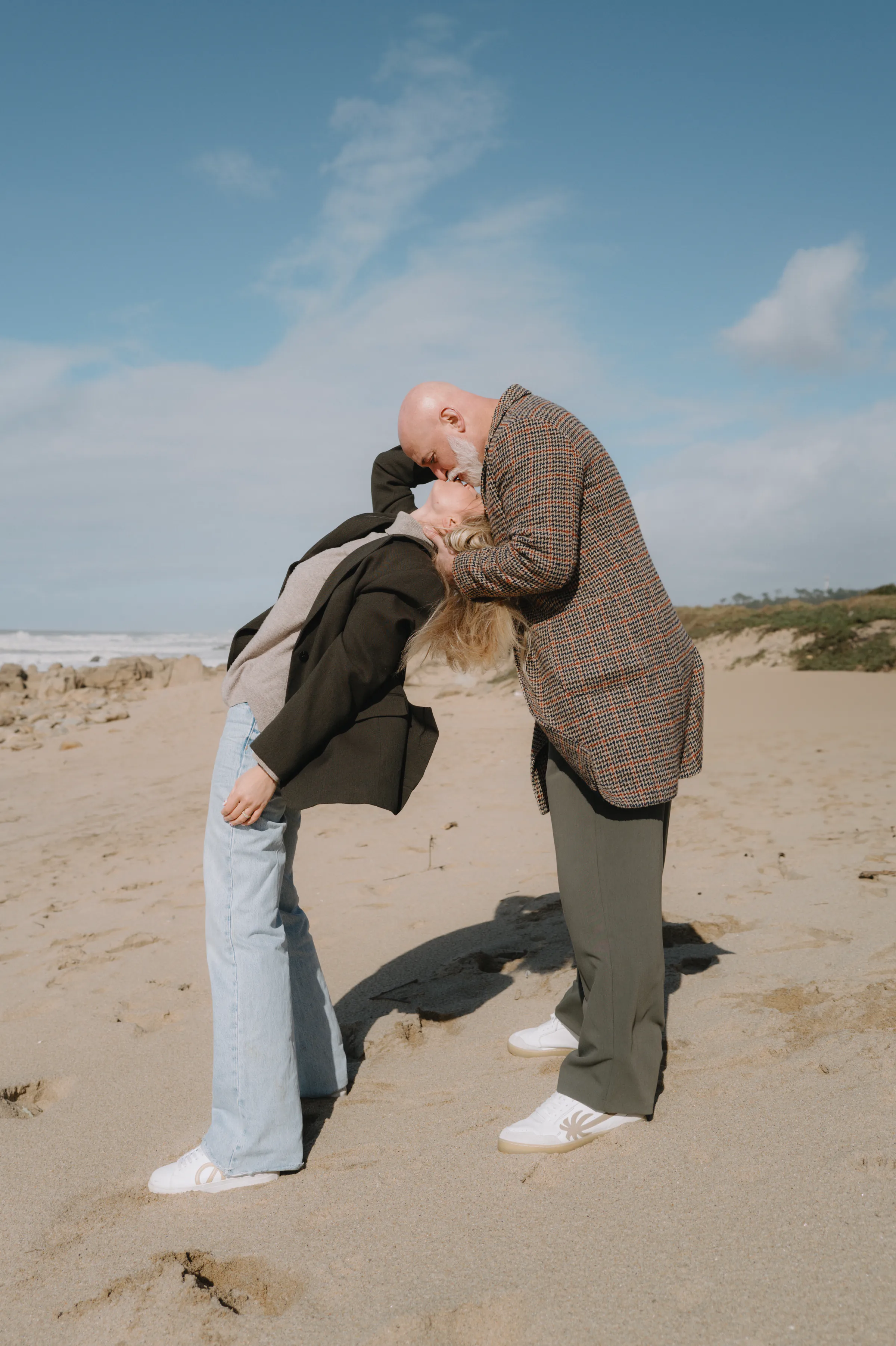 Couple leaning together on a sandy beach during a soft light seaside portrait session.