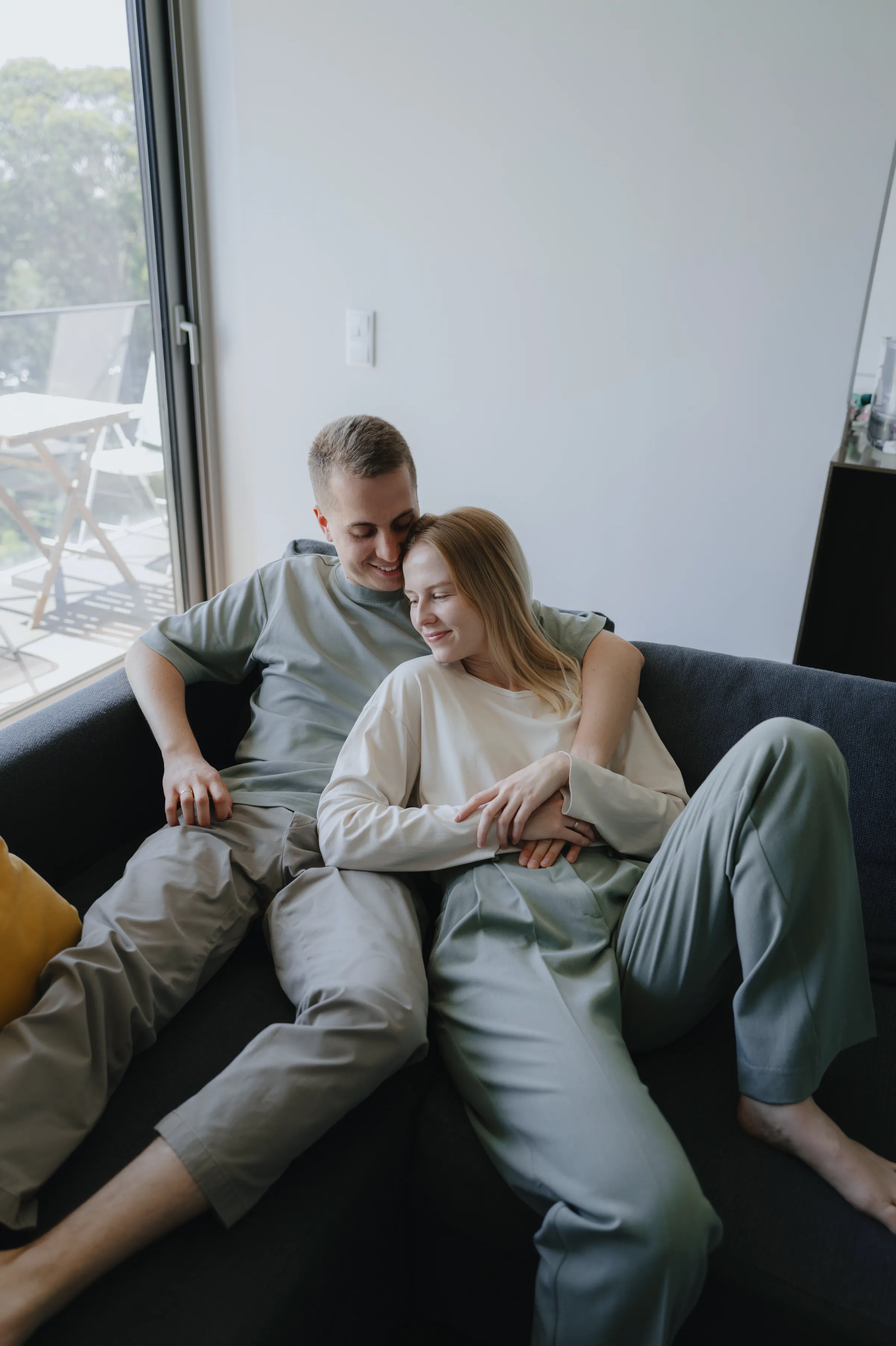Couple portrait on a sofa during a soft light home session by balcony doors.