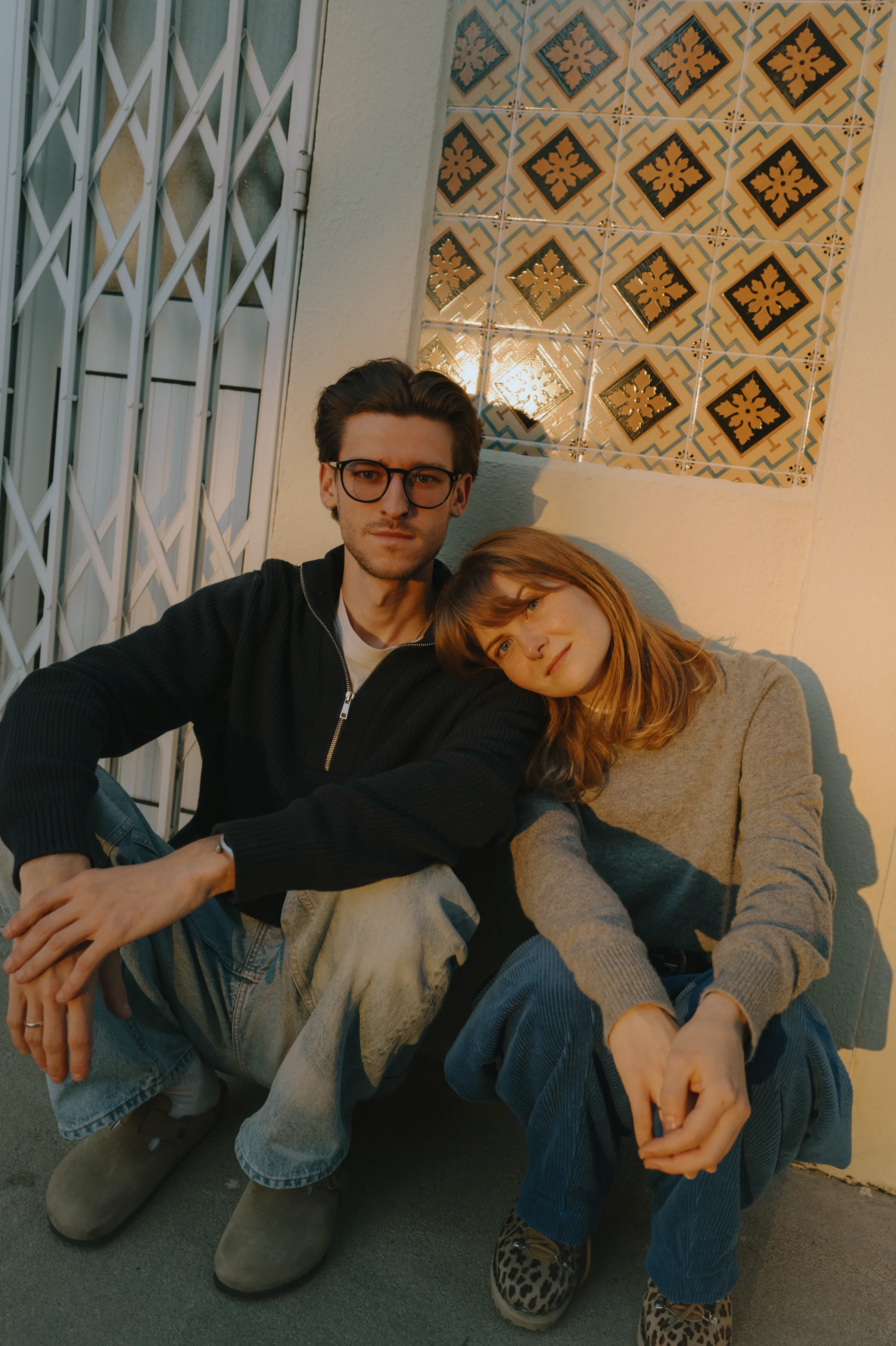 Couple portrait seated together by a tiled wall in warm soft light during an outdoor session