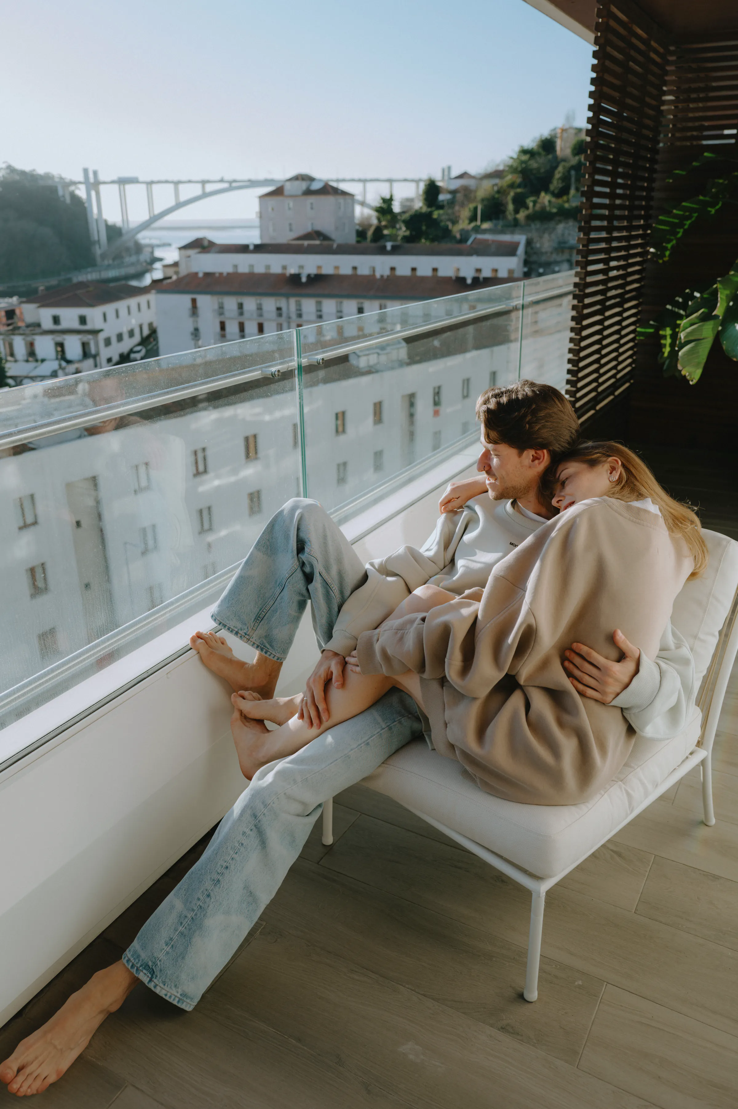 Couple portrait on a window lounge during a city session, with soft light and a bridge view.