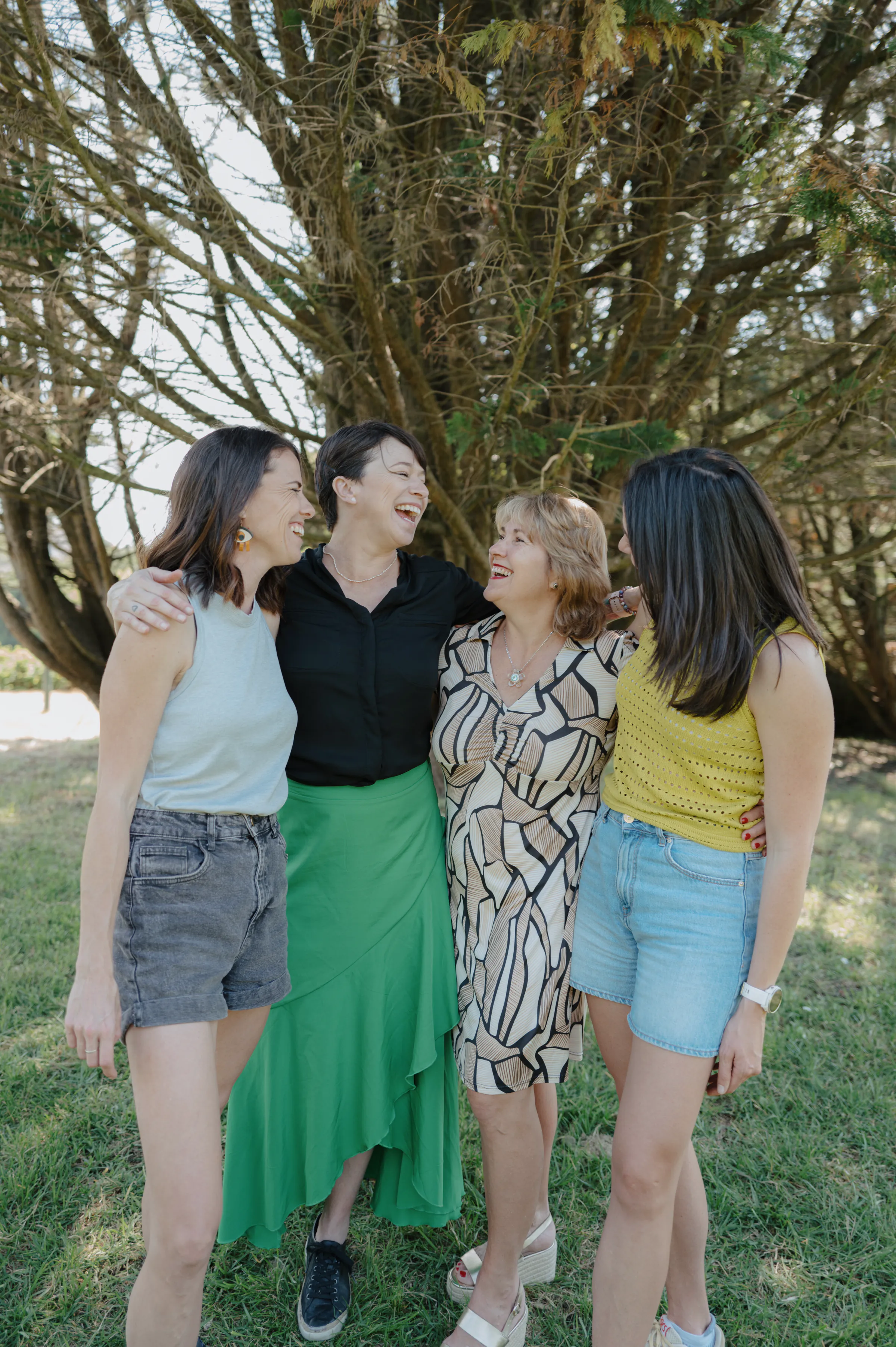 Outdoor group portrait of four people standing close together under trees in soft light.
