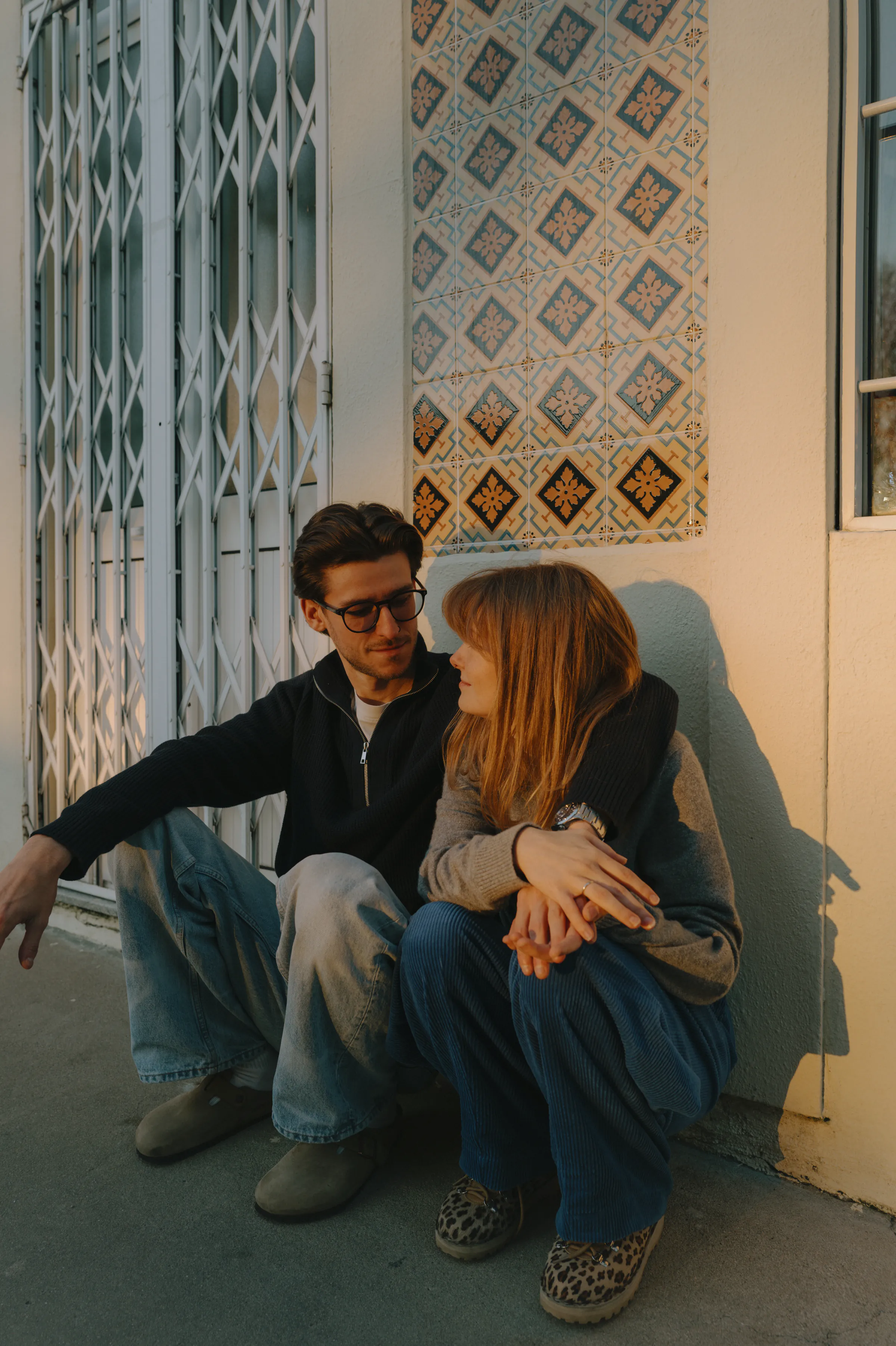 Couple seated close together on a city sidewalk during a warm, soft light outdoor session.