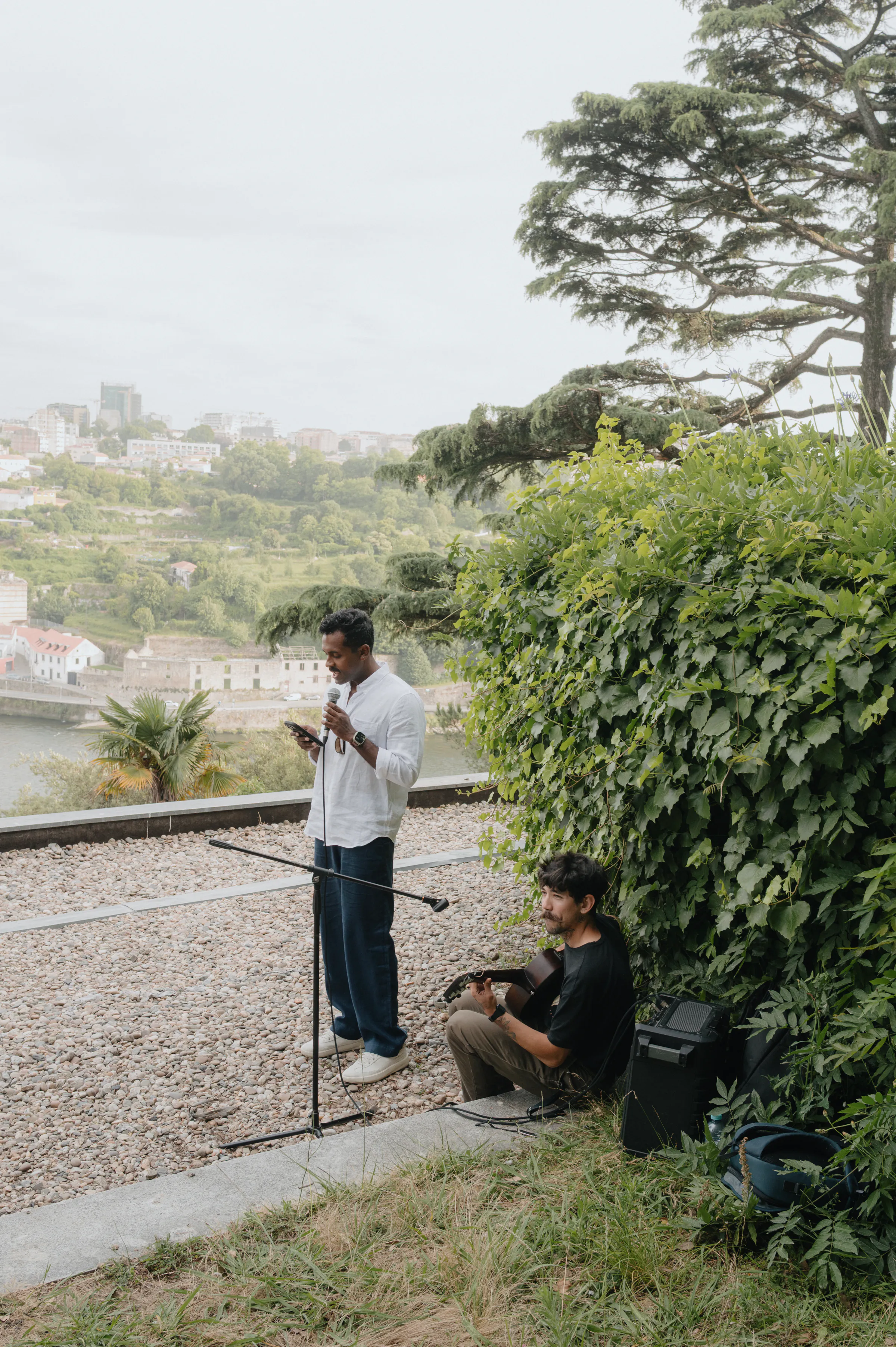 Outdoor session with two musicians performing on a garden terrace above a river and city view.