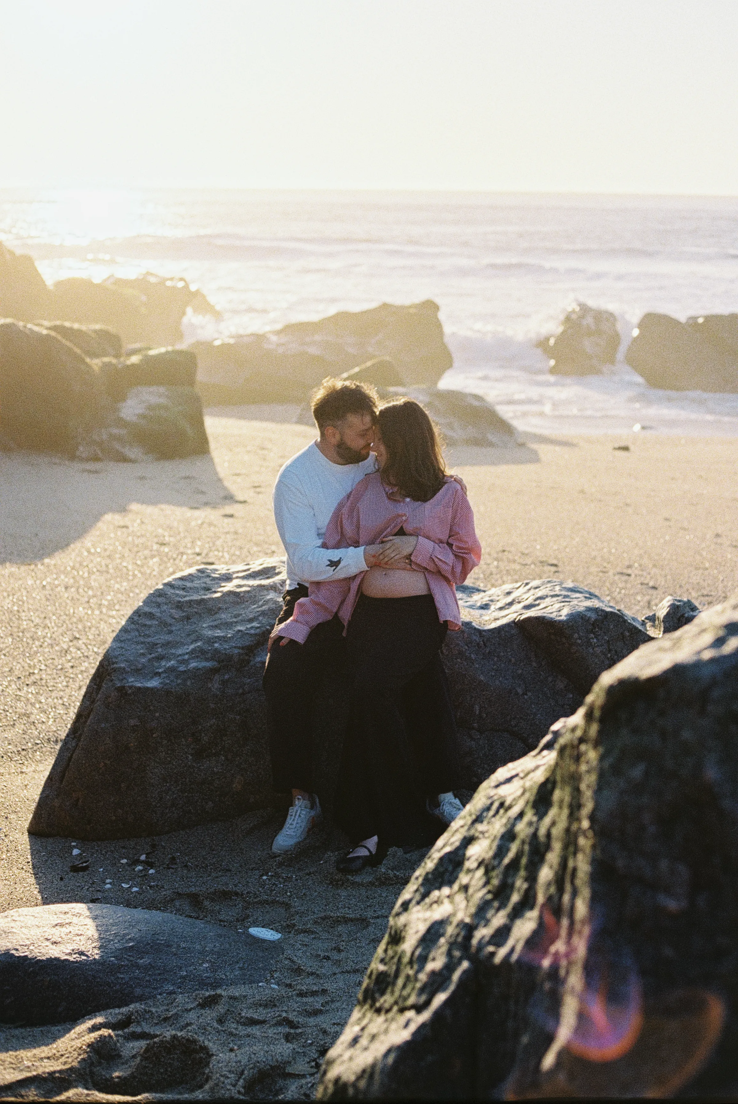 Couple seated on beach rocks during a seaside session in soft light.