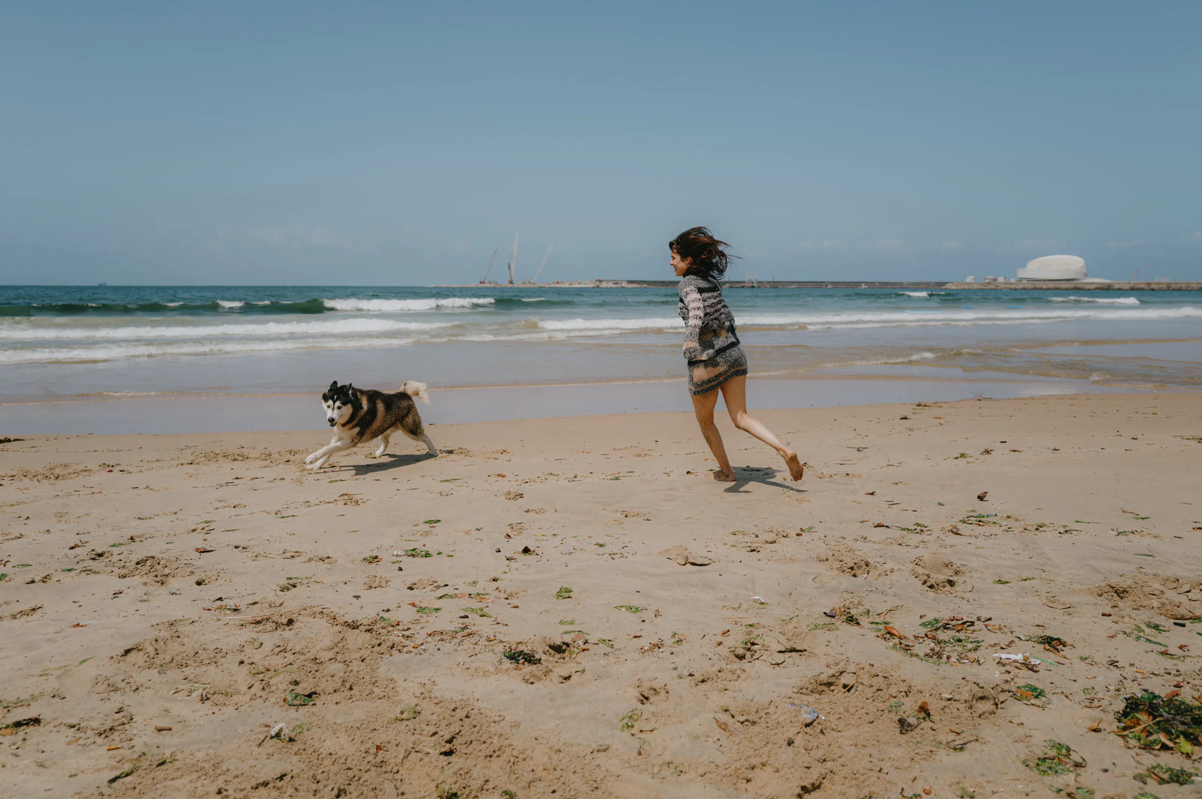 Child running with a dog during a seaside outdoor session on a sandy beach.