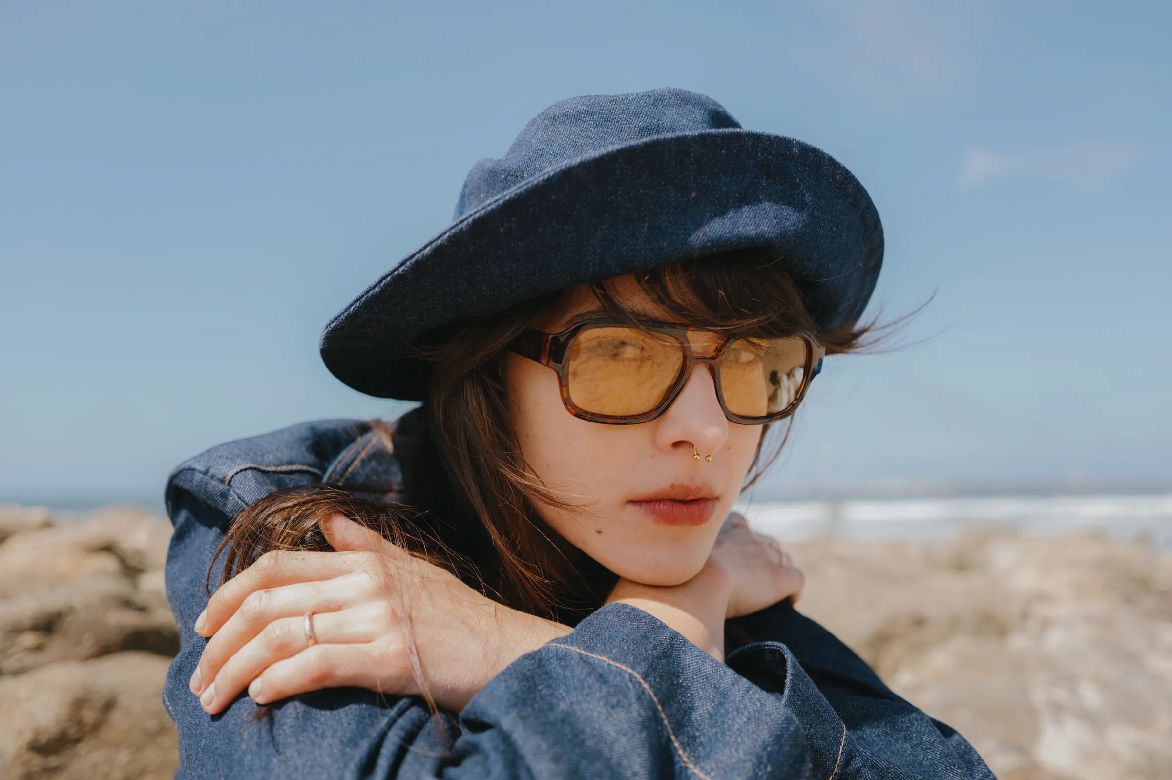 Close portrait of a couple at the seaside, one wearing glasses and a wide-brim hat.