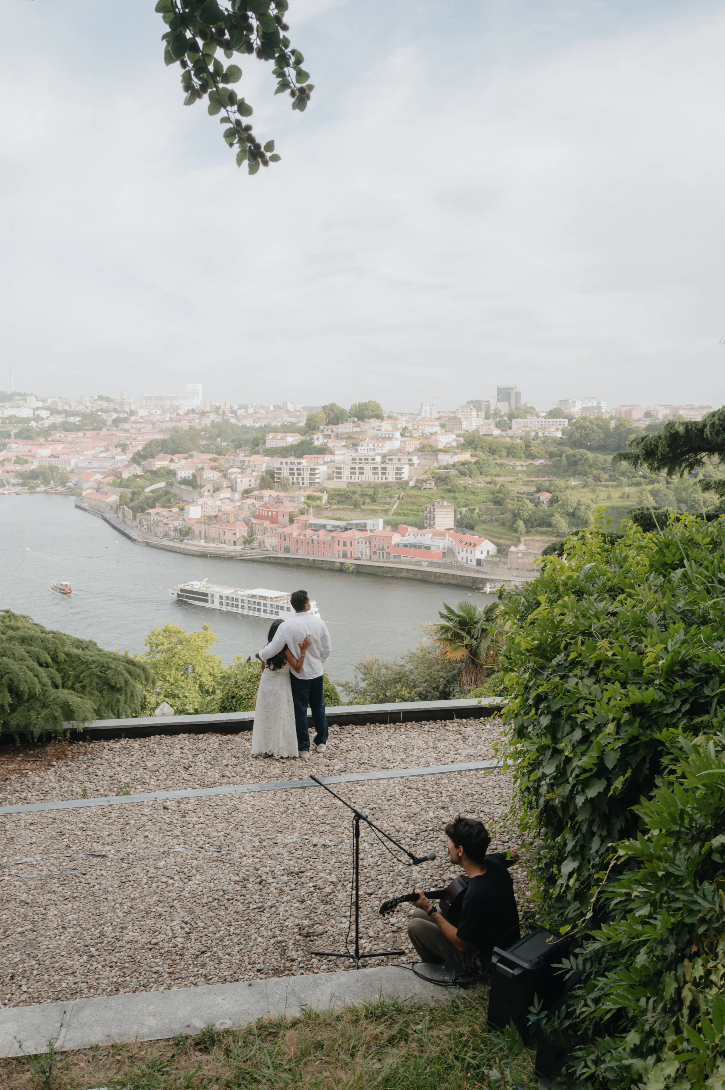 Couple during an outdoor session overlooking a river and city, with soft light and greenery around them.