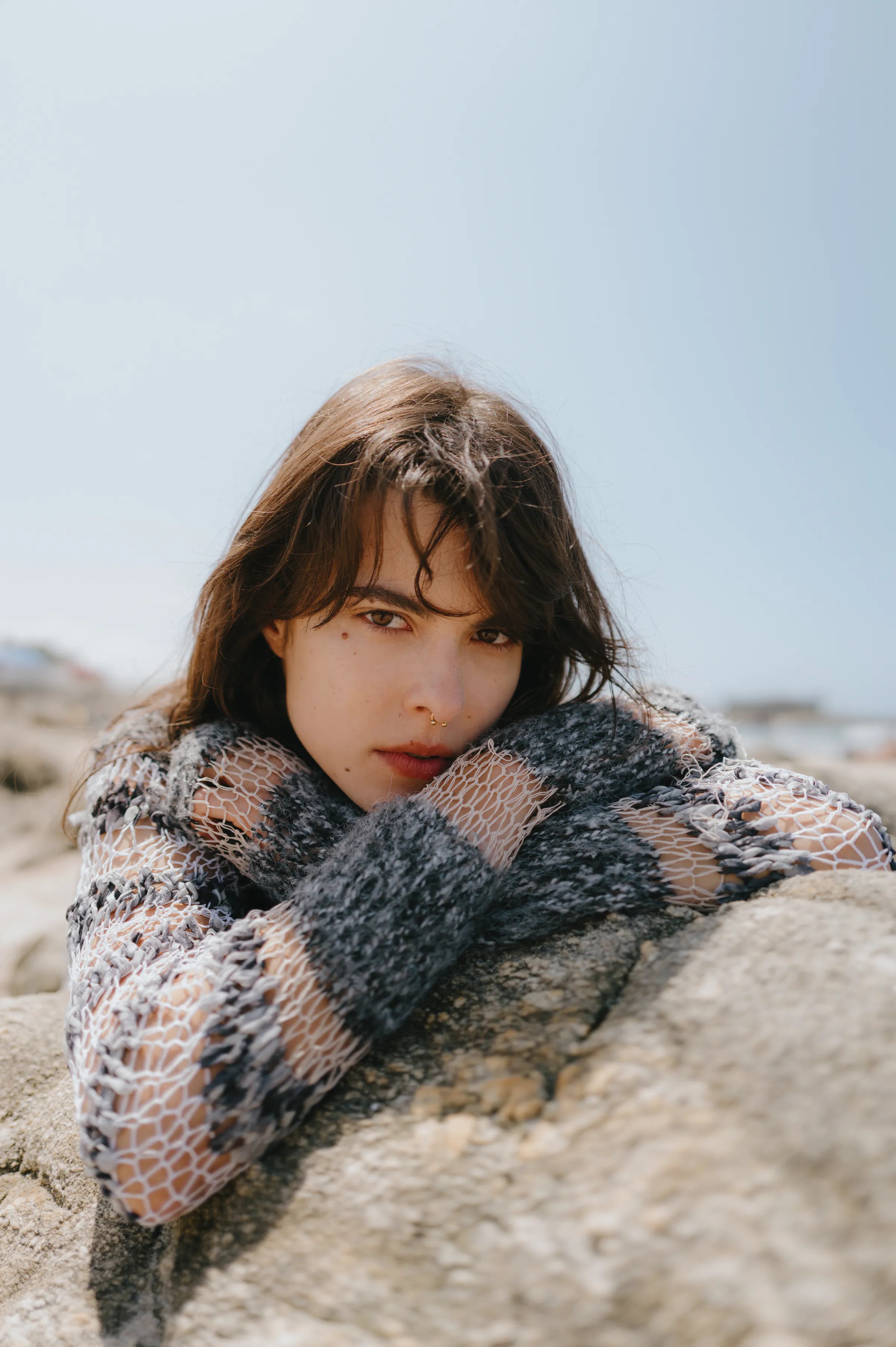 Close portrait of a person leaning on seaside rocks in soft light, wearing a textured knit sweater.