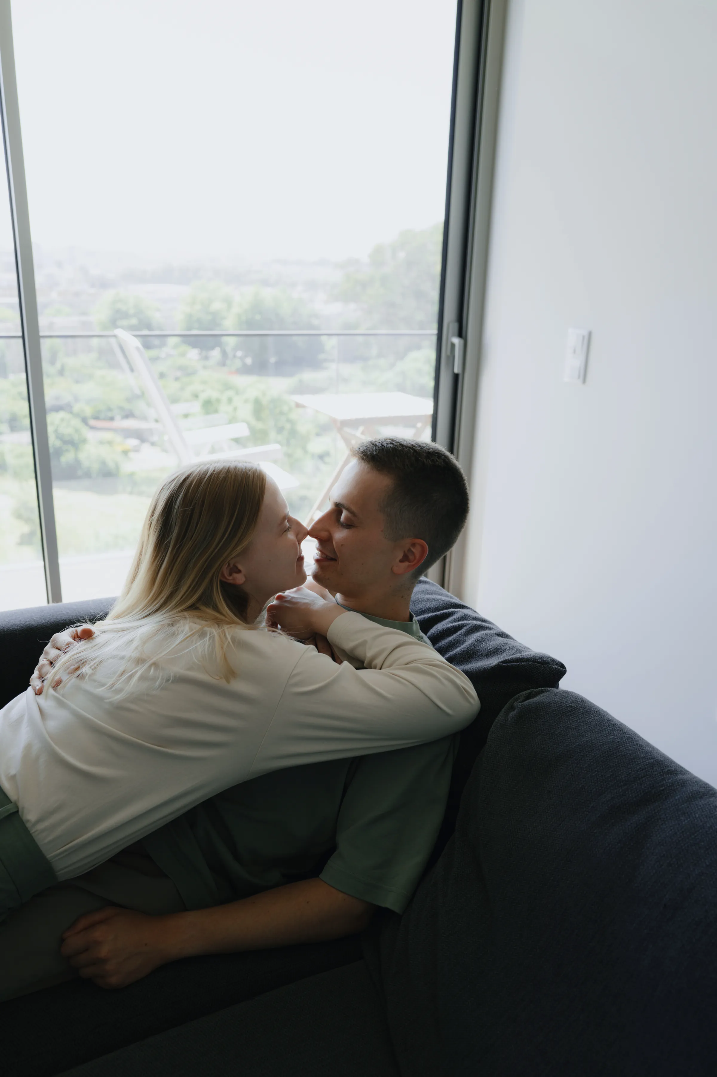 Couple sharing a close portrait on a couch beside a bright window during a home session.