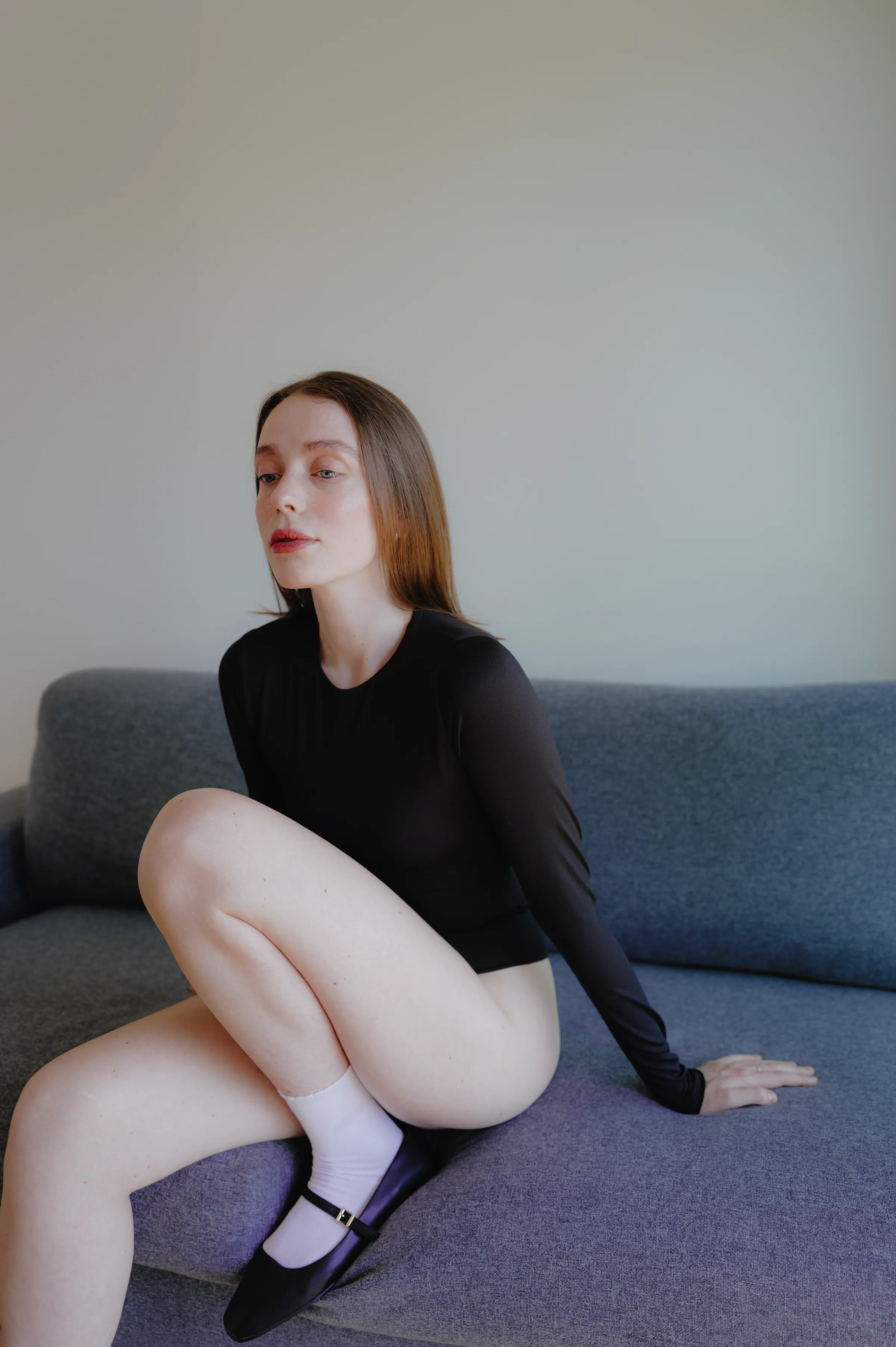 Indoor portrait of a woman seated on a gray sofa in soft light.