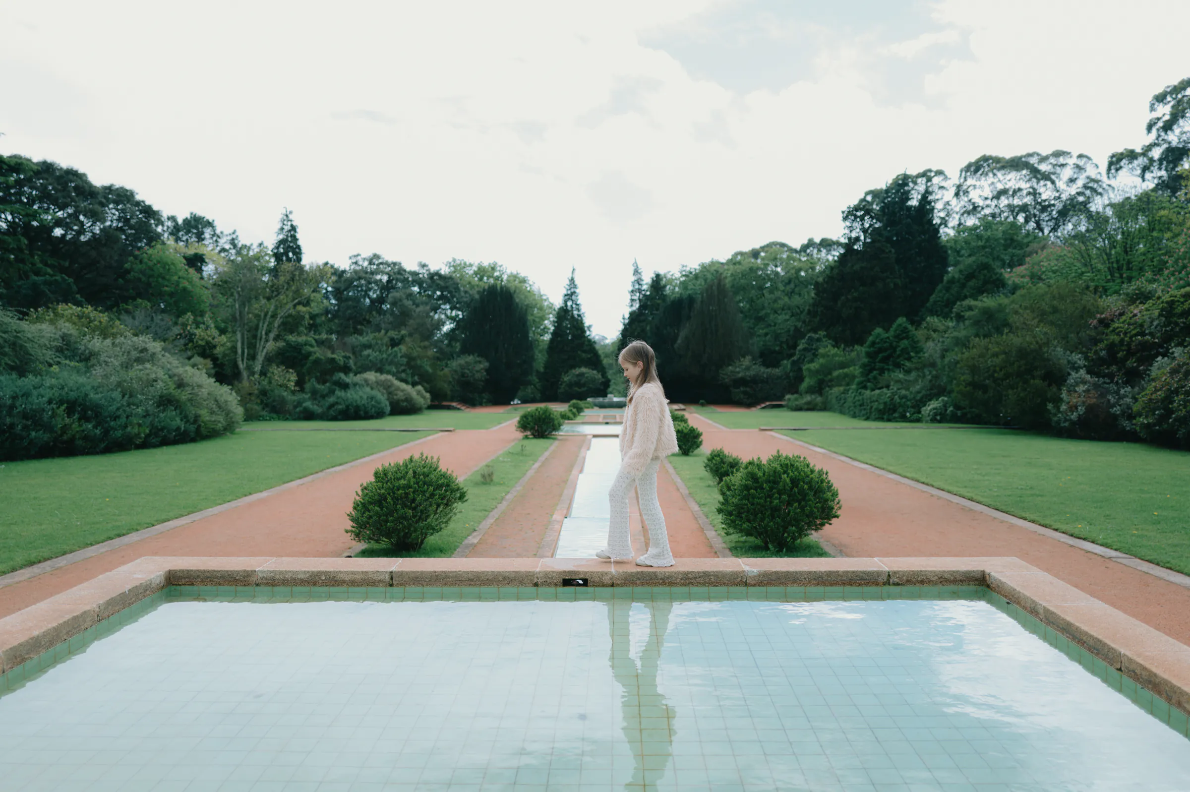 Person walking beside a reflecting pool during a garden outdoor session in soft light.
